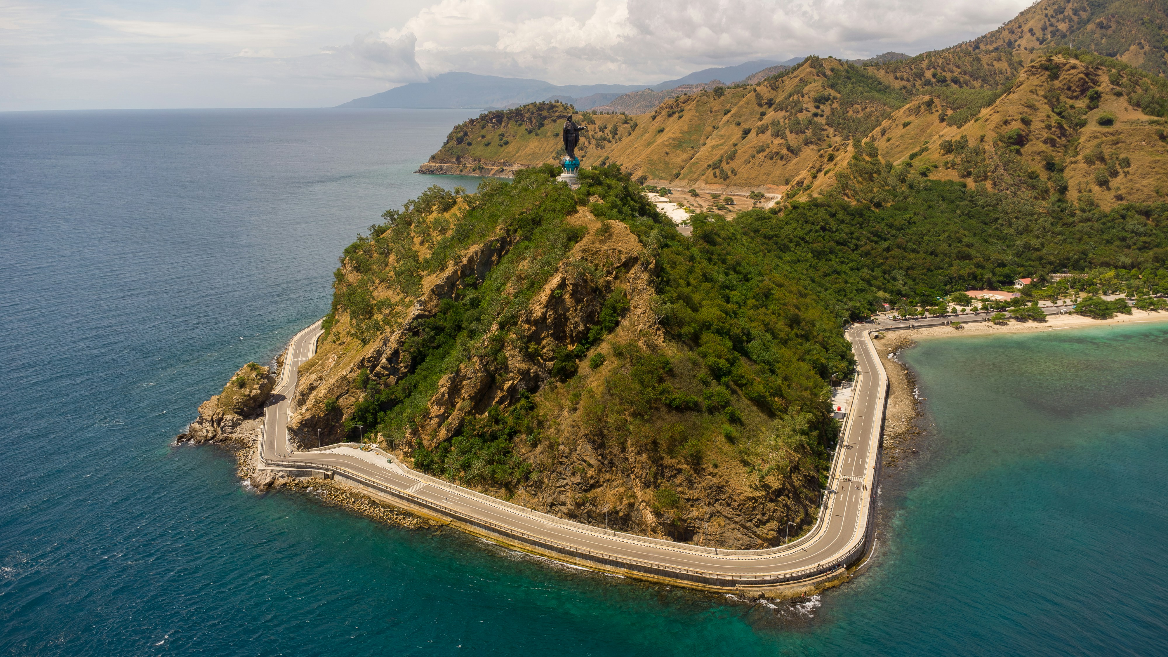 A coastal road winds along a verdant mountain.