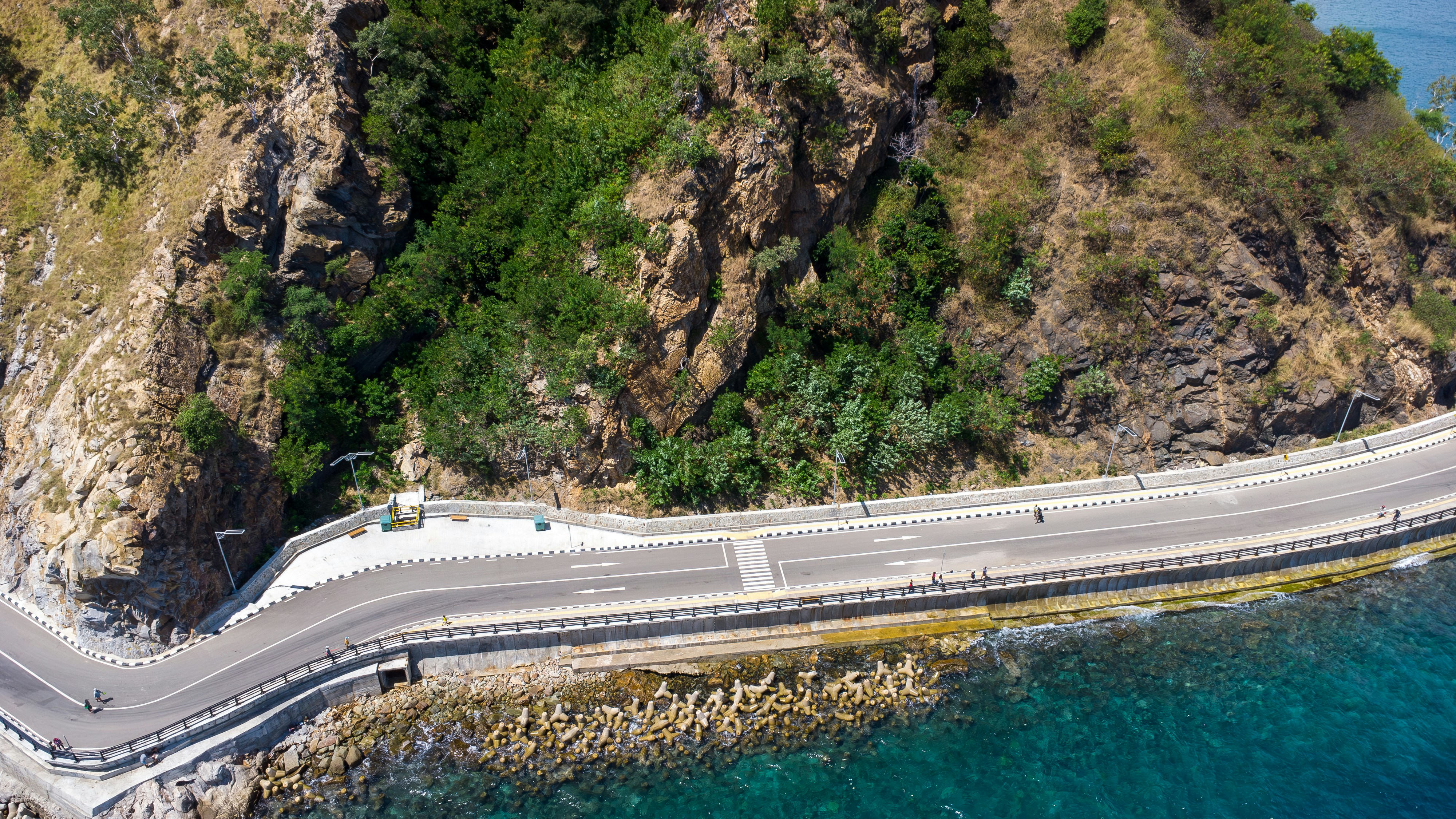 A coastal road winds alongside a rocky cliff.
