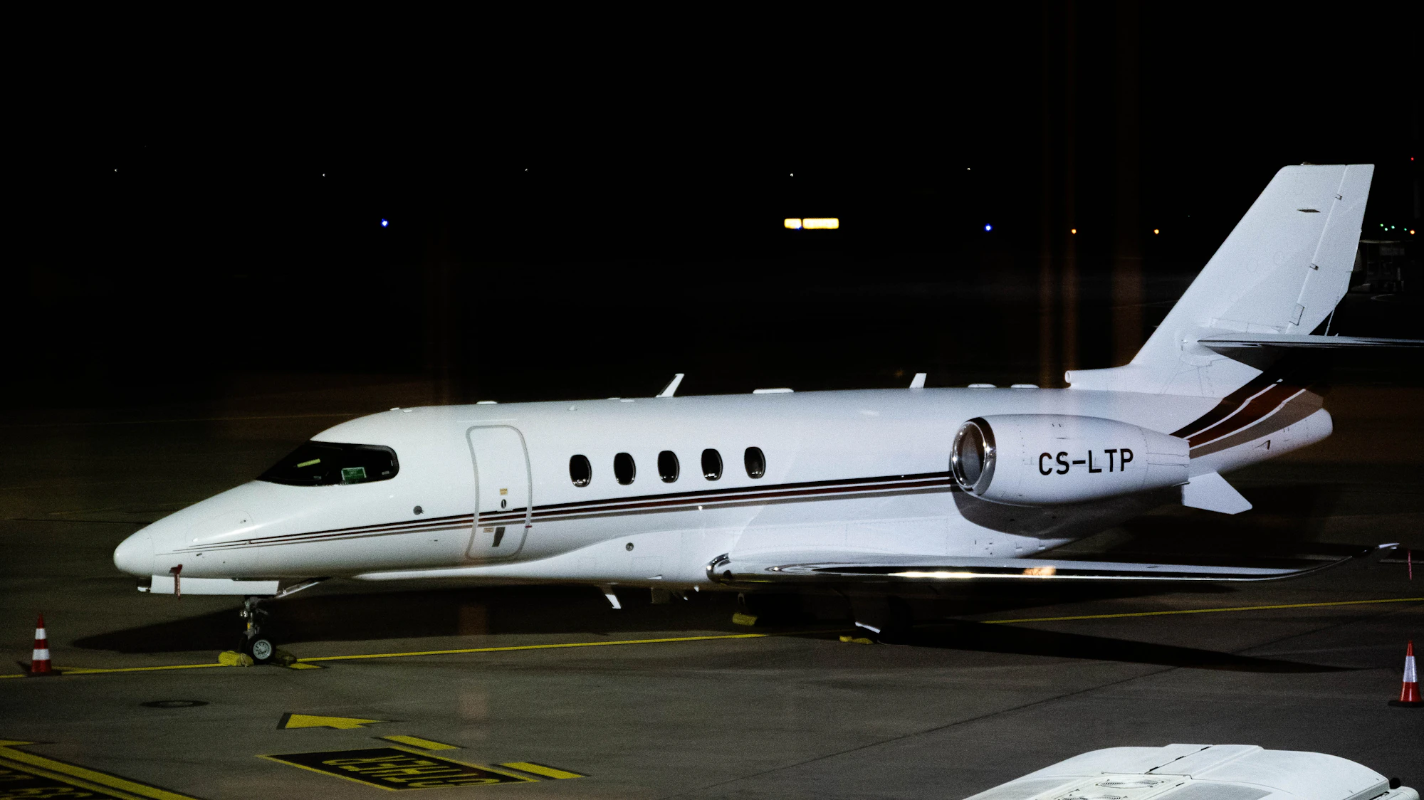 A midsize business jet parked on a floodlit apron at night, the kind of aircraft behind a typical midsize jet charter cost