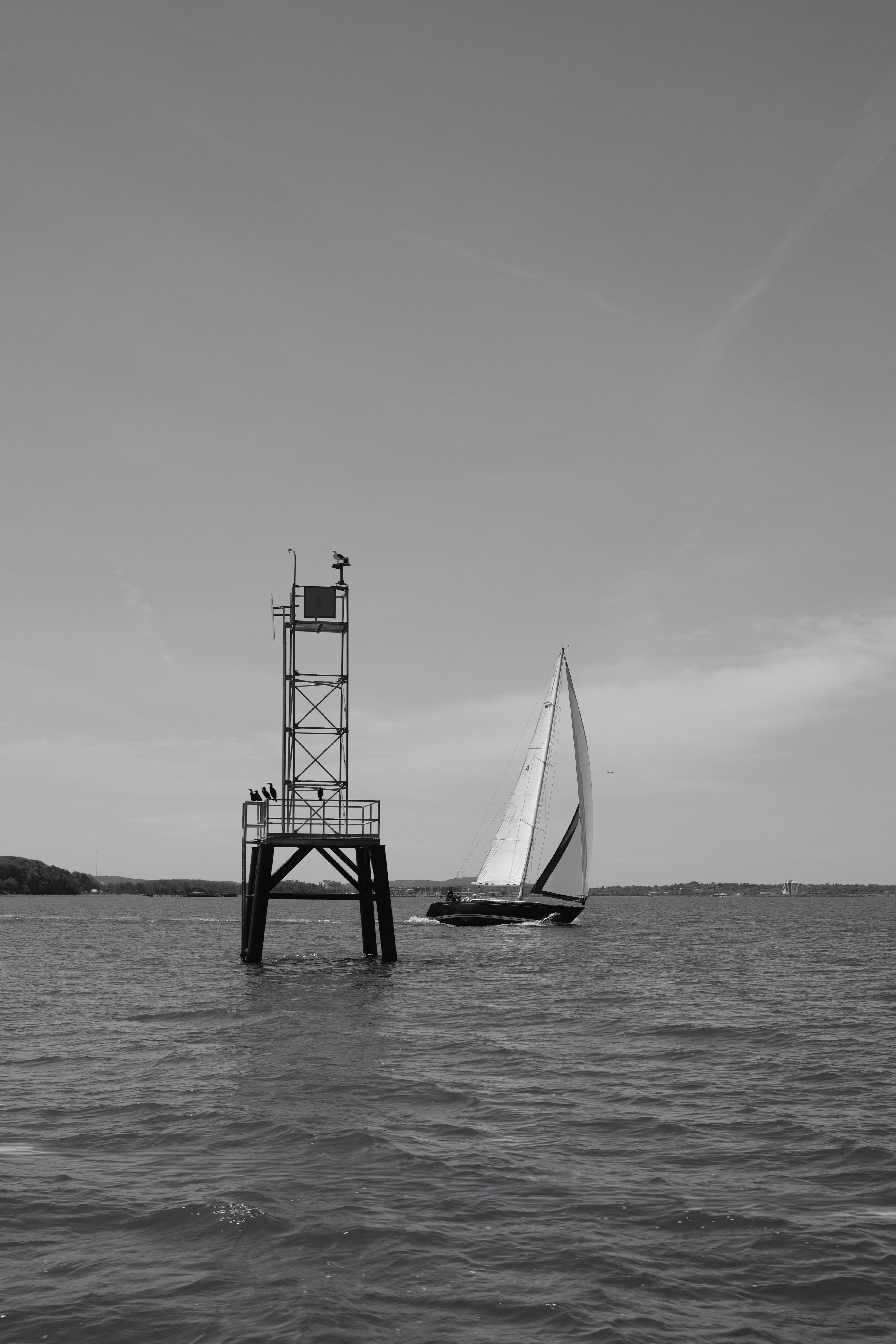 Sailboat sails past a navigational marker on the water.