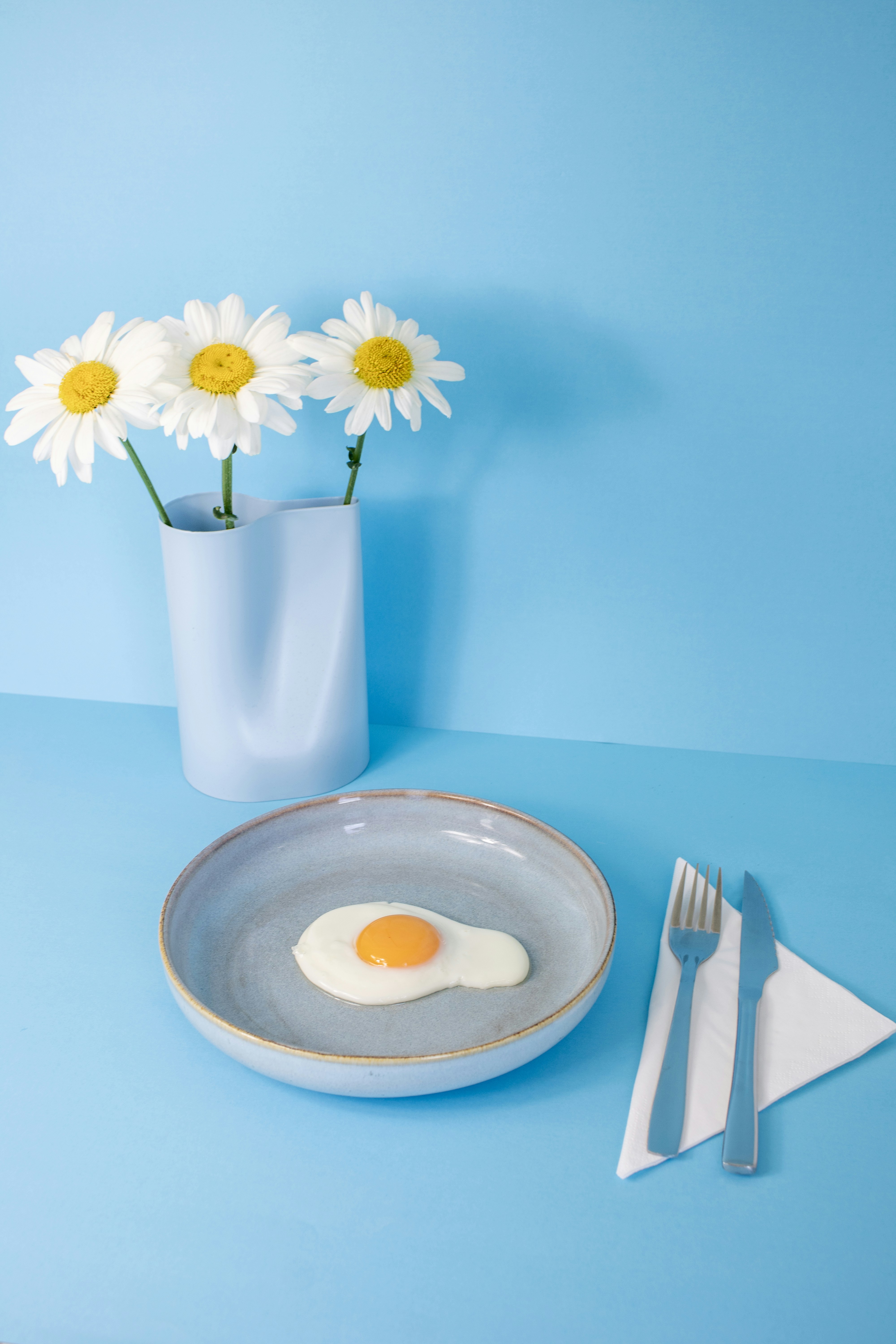 Fried egg, flowers, and cutlery on a blue surface.