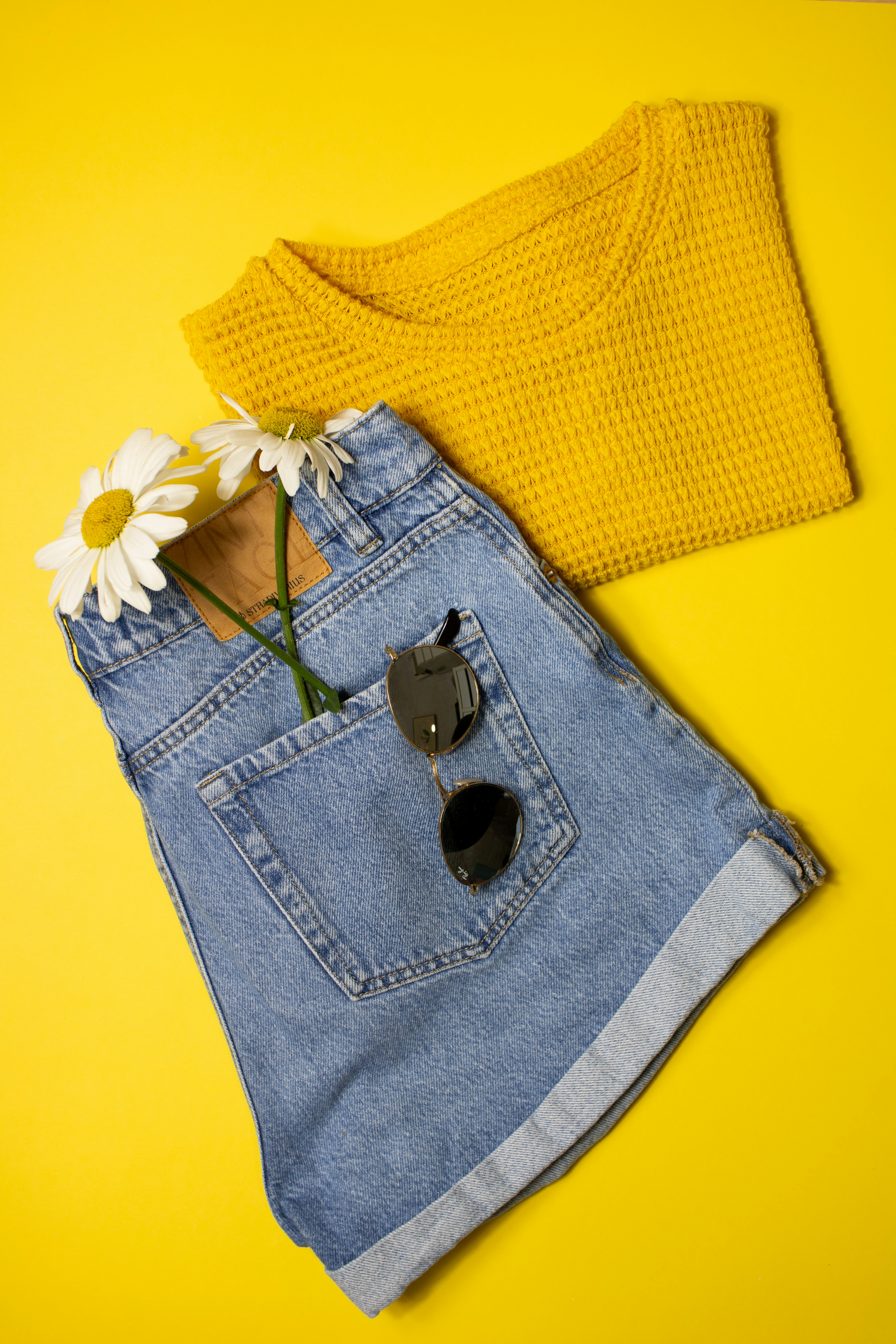 Denim shorts and yellow top on a yellow surface.