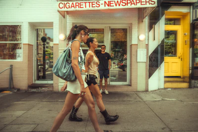 Two women walk past a store on a sunny day.