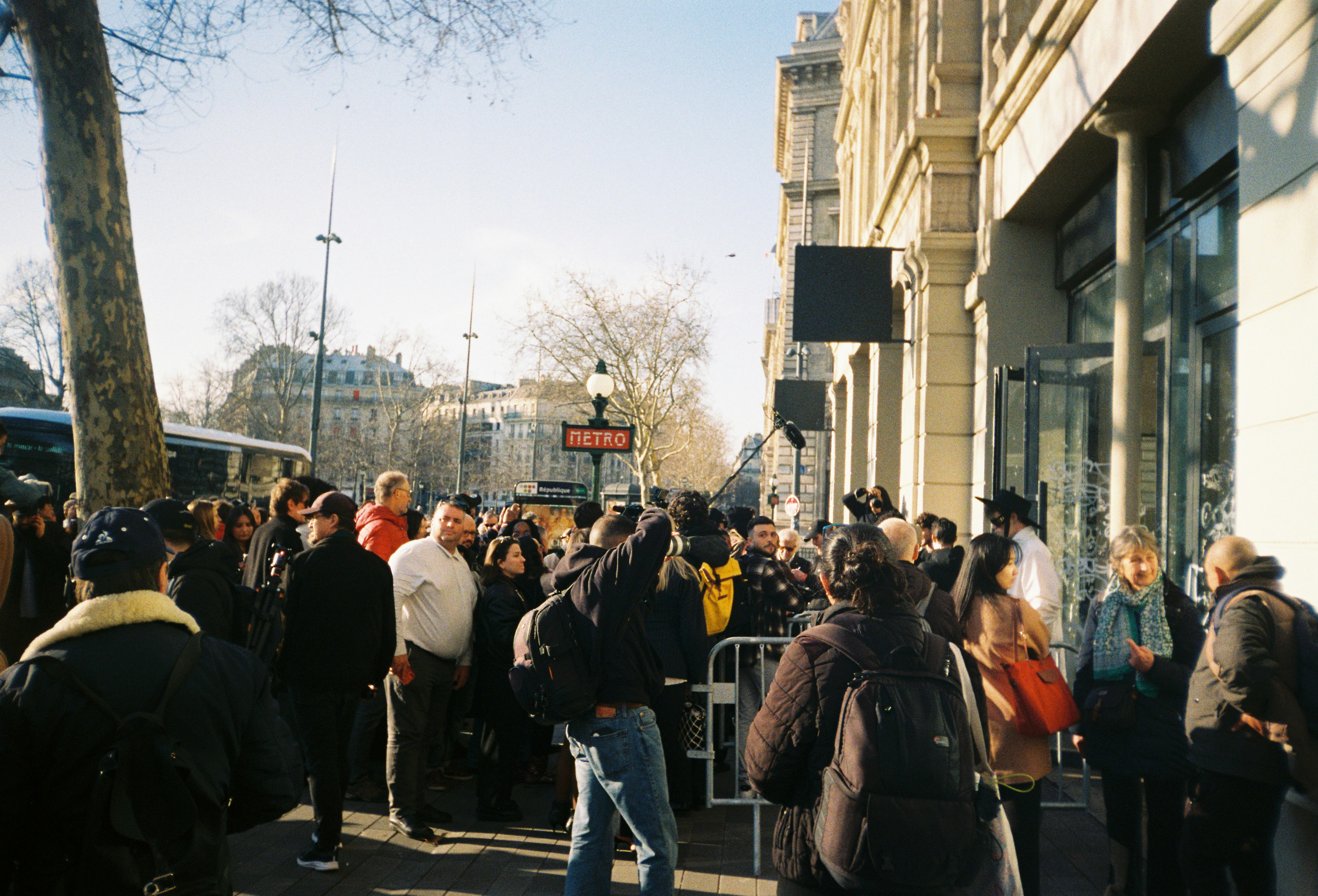 People queueing on a sunny street.