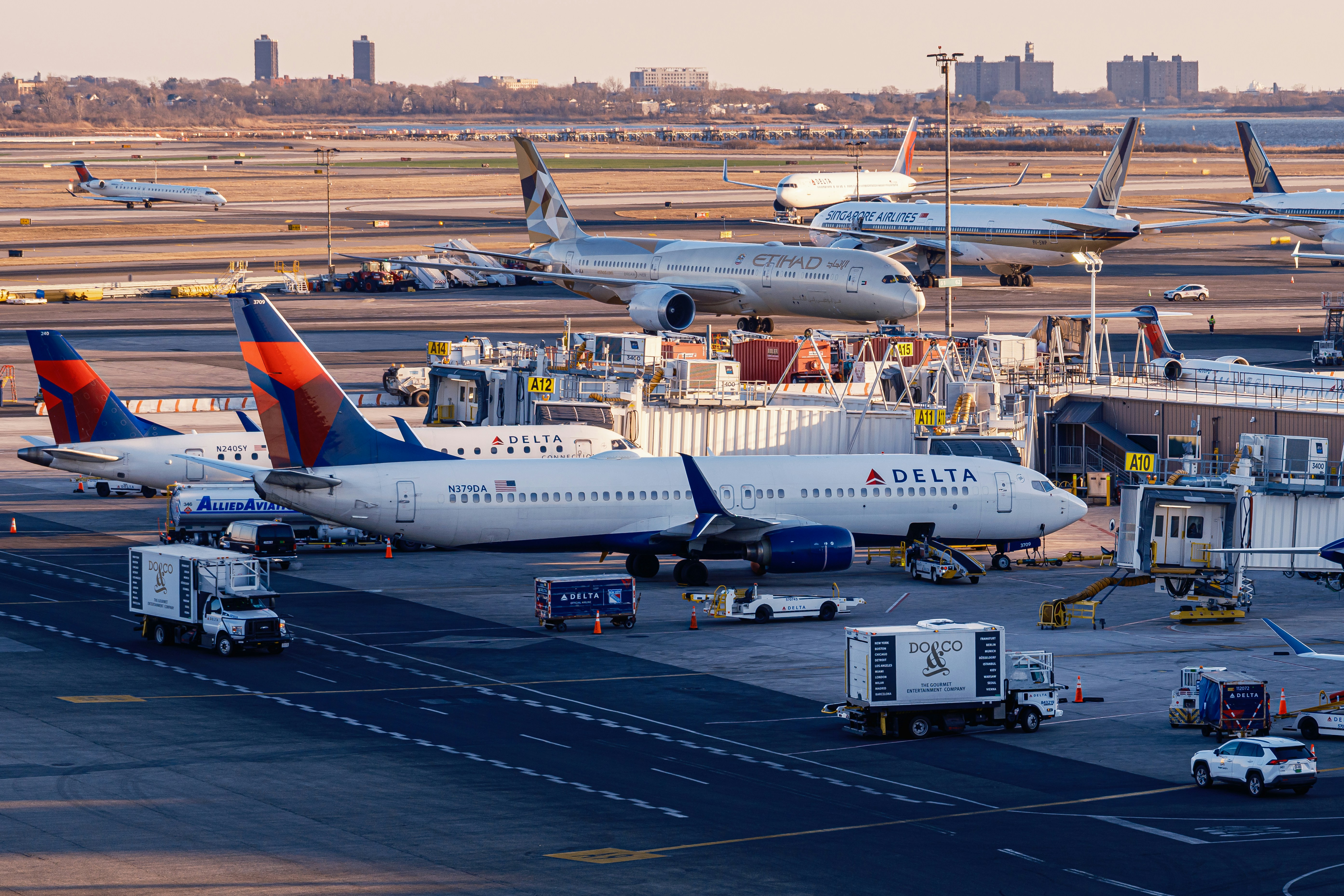 Airplanes are parked at a busy airport terminal., Editorial image of Delta, Etihad, and Singapore Airlines aircraft on the apron at JFK Airport, viewed from the TWA Hotel rooftop, New York City, New York, United States