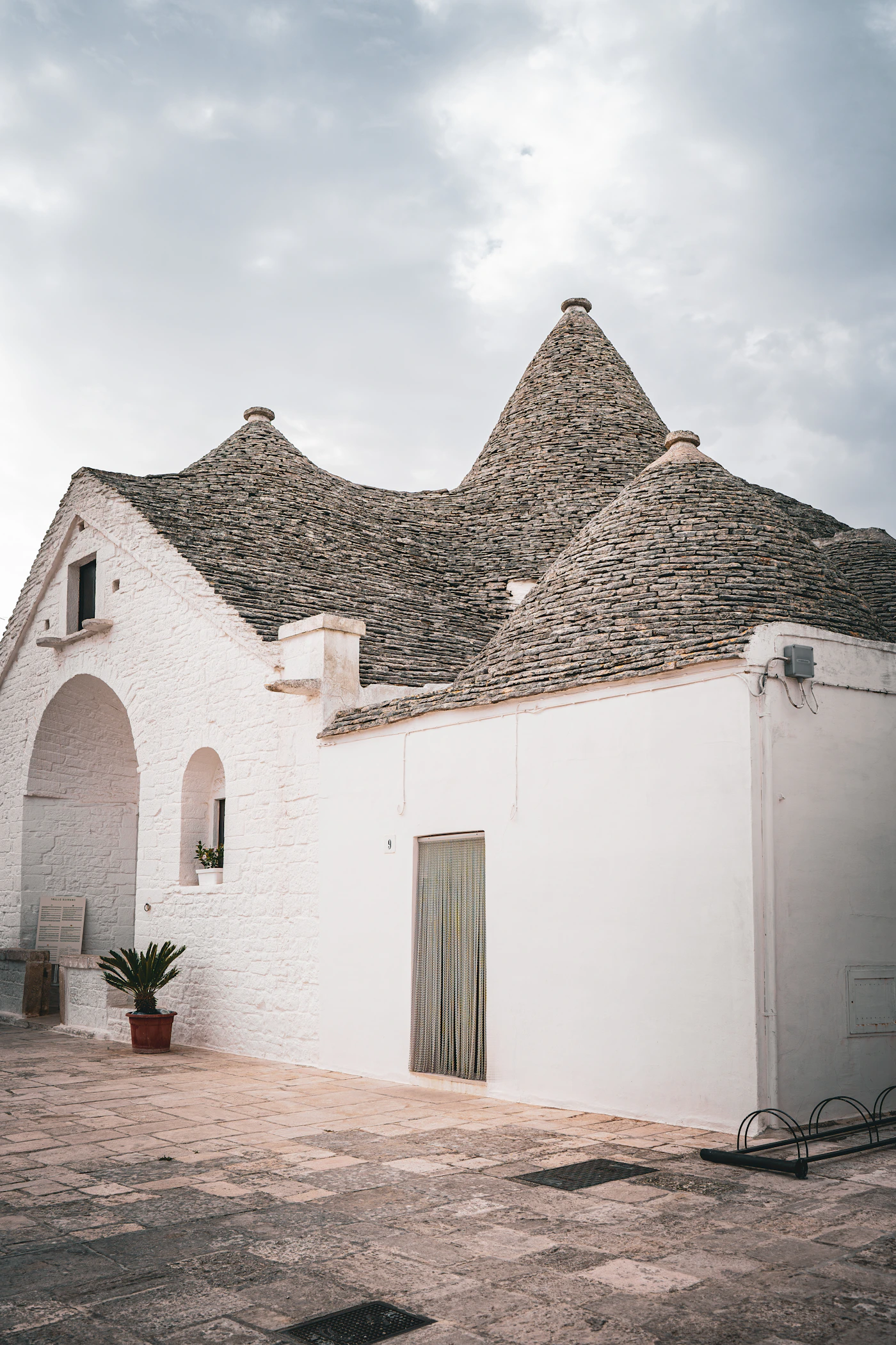 A row of traditional trulli houses in Puglia Italy with their distinctive conical stone roofs surrounded by purple wildflowers and green grass under a soft sky