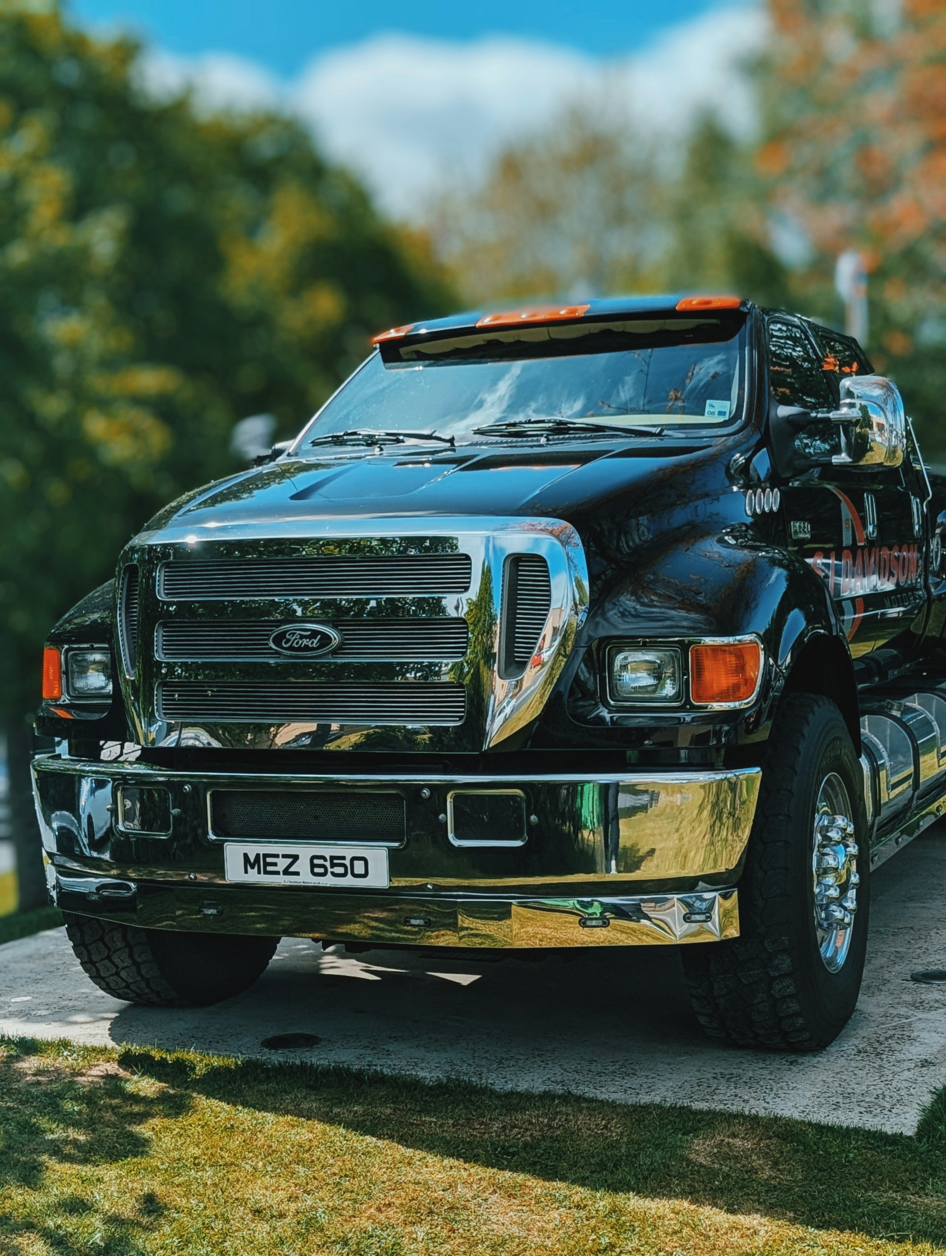 A shiny black ford tow truck with chrome accents and the license plate mez 650 is parked outdoors on a sunny day, set against green trees and a blue sky—perfect for those considering tow truck leasing.