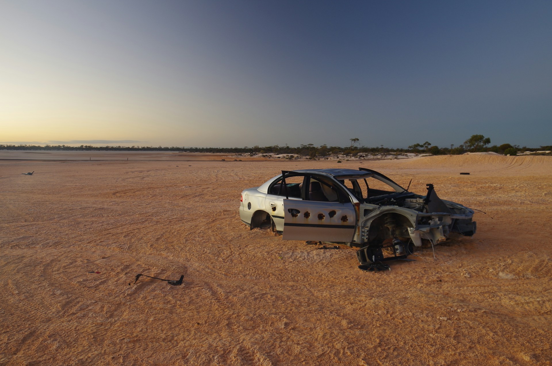 A wrecked car sits alone in a barren landscape.