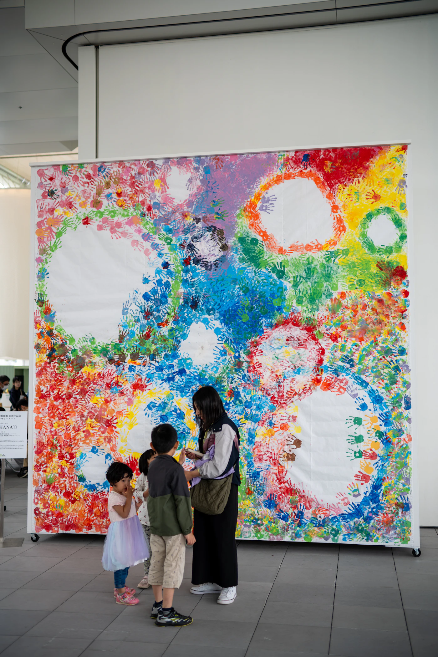 Children and an adult thoughtfully viewing a colorful finished artwork