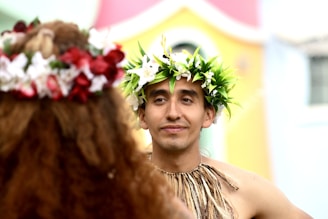 Two people wear flower crowns, smiling and facing forward.