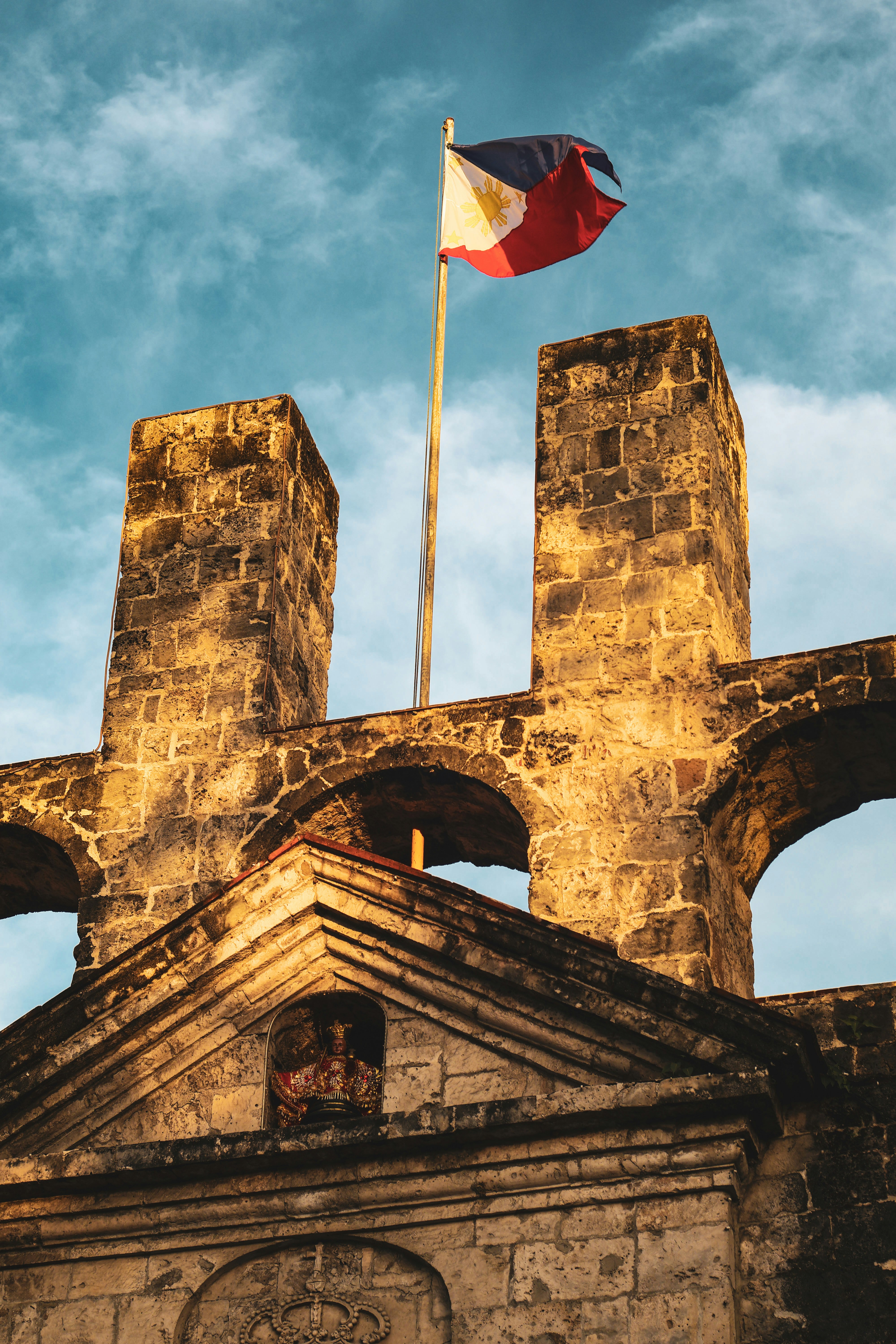 The philippine flag flies over an old stone structure.