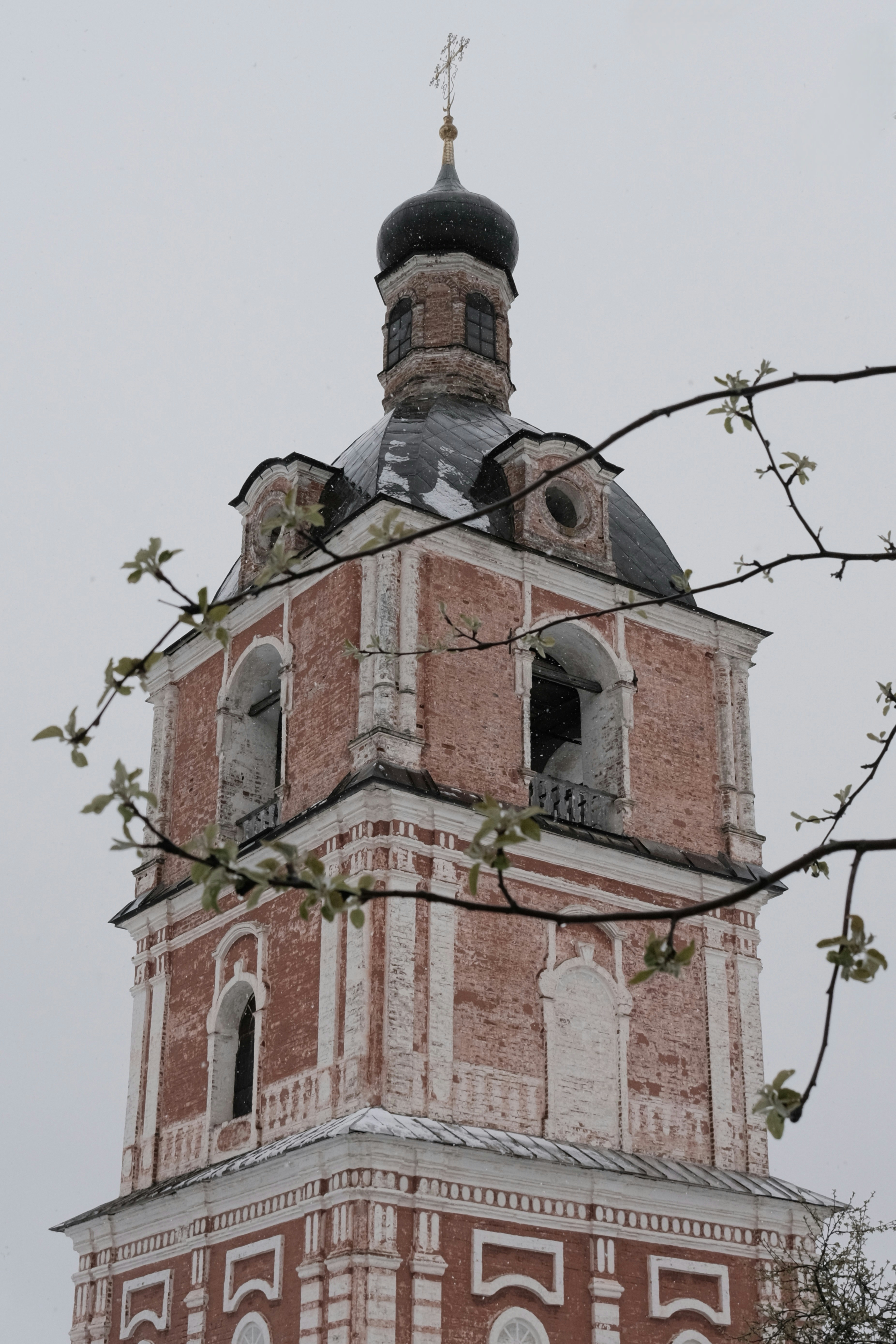 A tall brick church tower reaches into the cloudy sky.