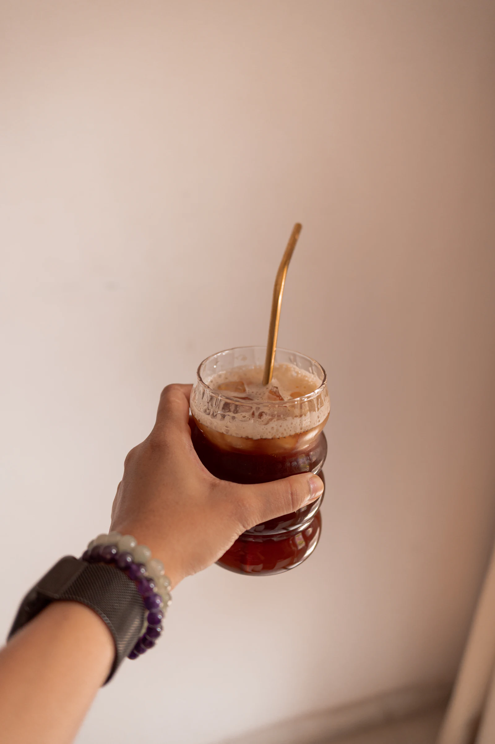 A hand holding a tall glass of iced coffee with a straw