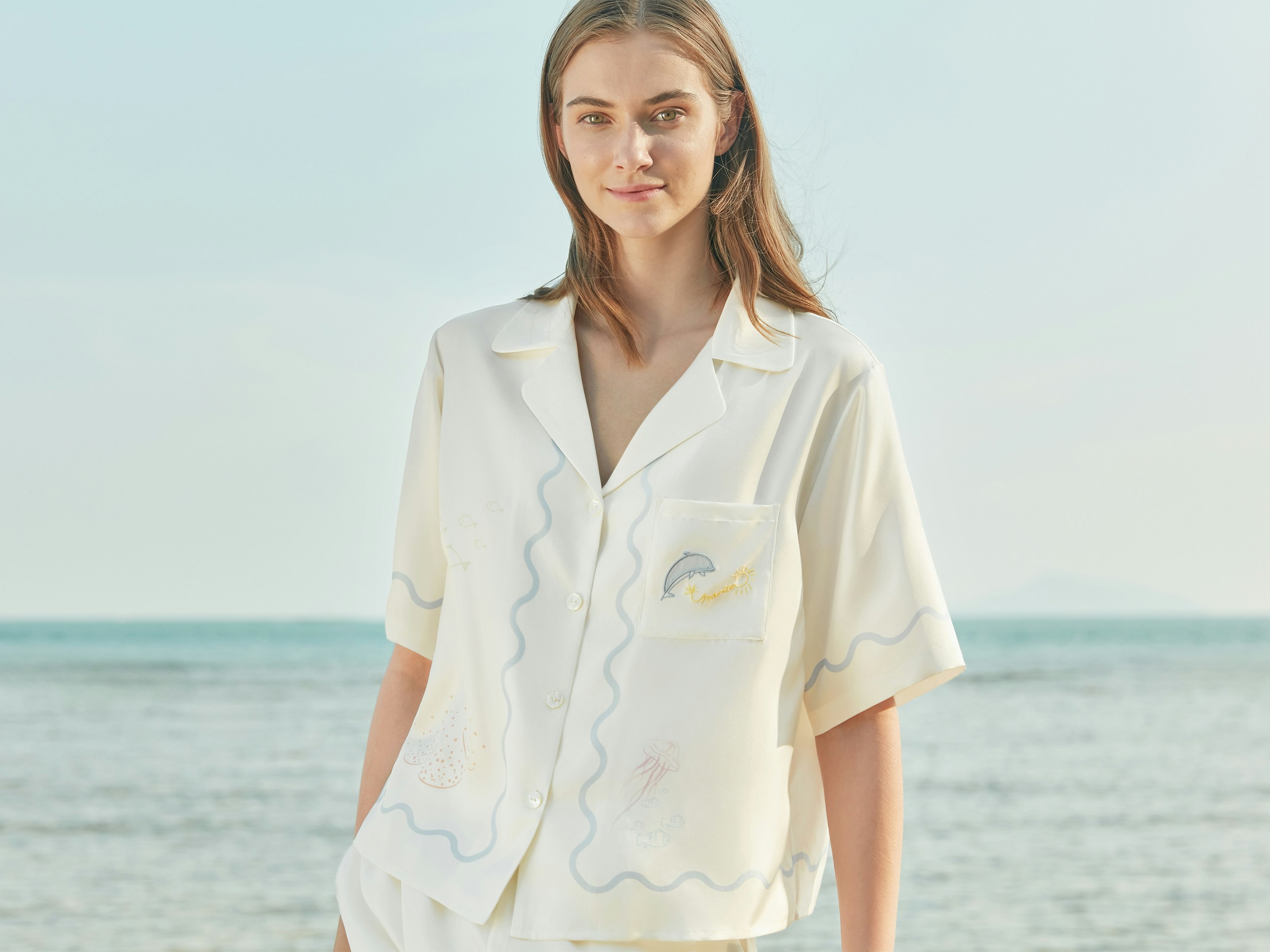 Soft smiles and seaside breeze—model in MANITO white embroidered silk set by the water.