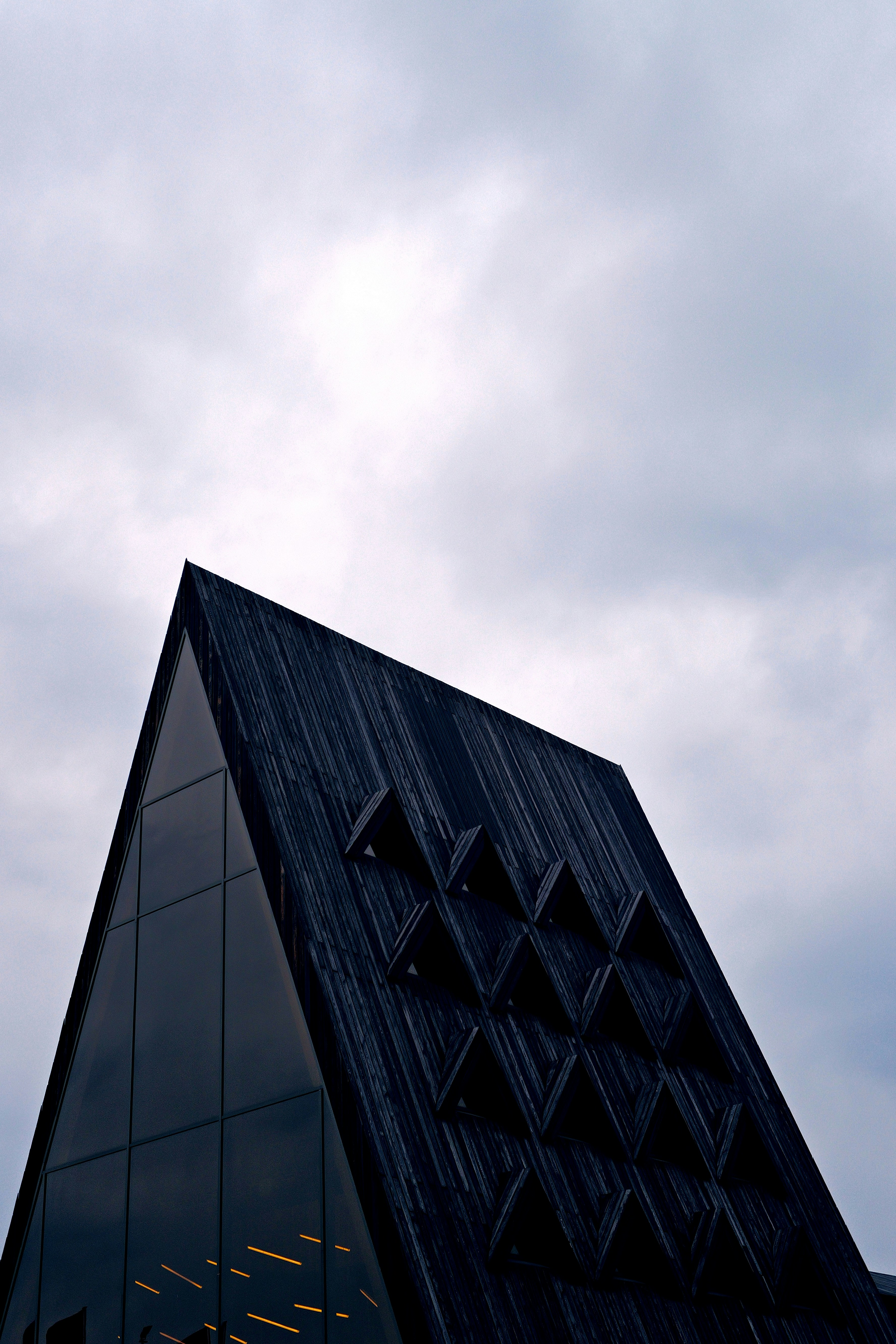 Architectural details of a wooden, triangular building under cloudy skies.