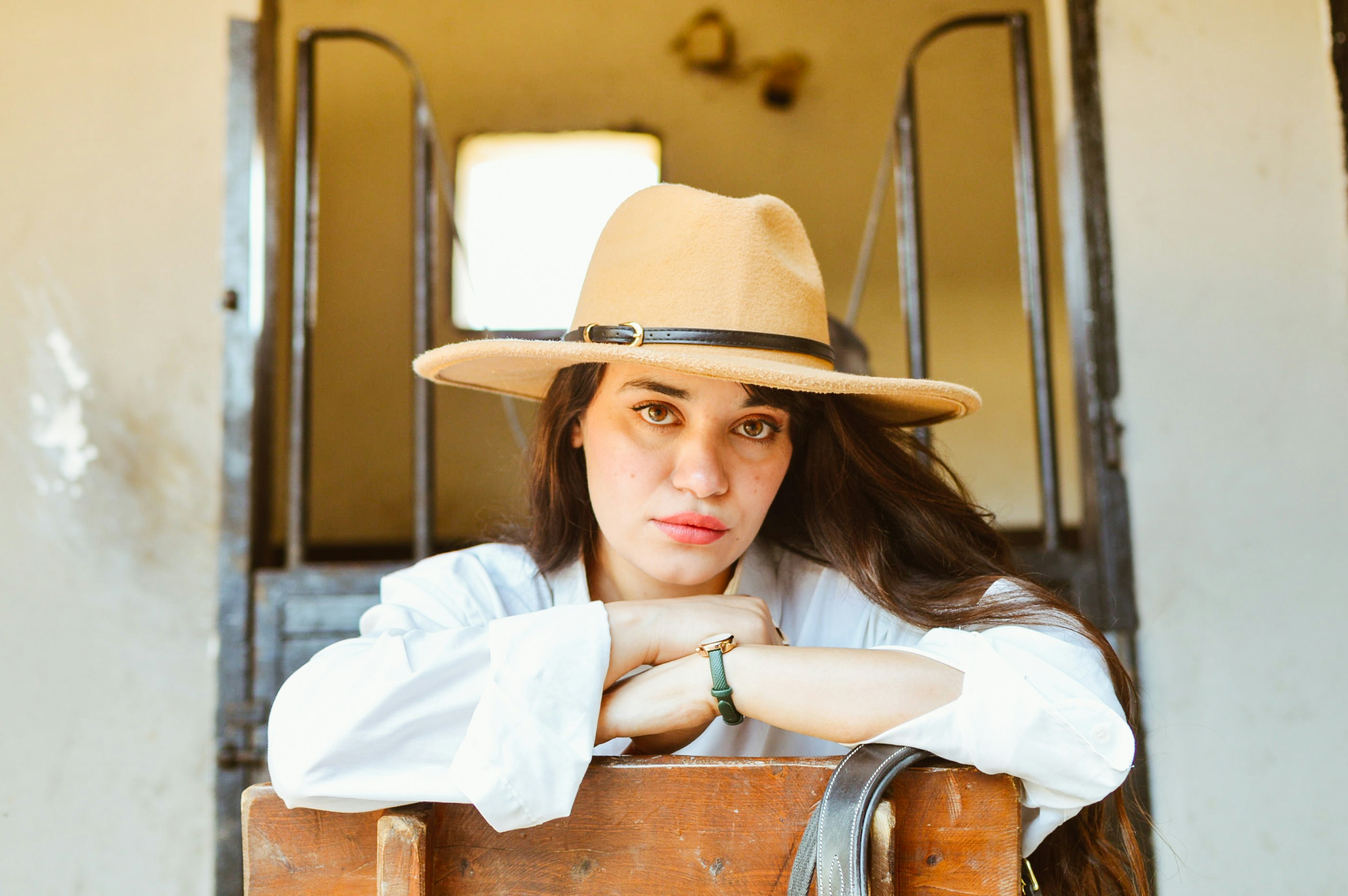 Mulher em poses de chapéu, apoiando-se em uma superfície de madeira.