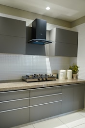 Модерна кухня със сиви шкафове и малък бял гръб от плочки зад плота.