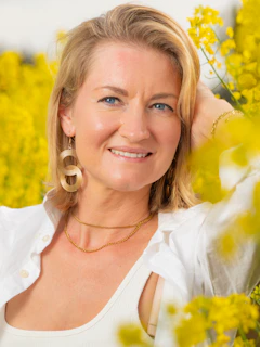 A woman smiles amidst yellow flowers.