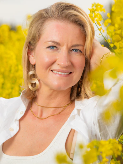A woman smiles amidst yellow flowers.