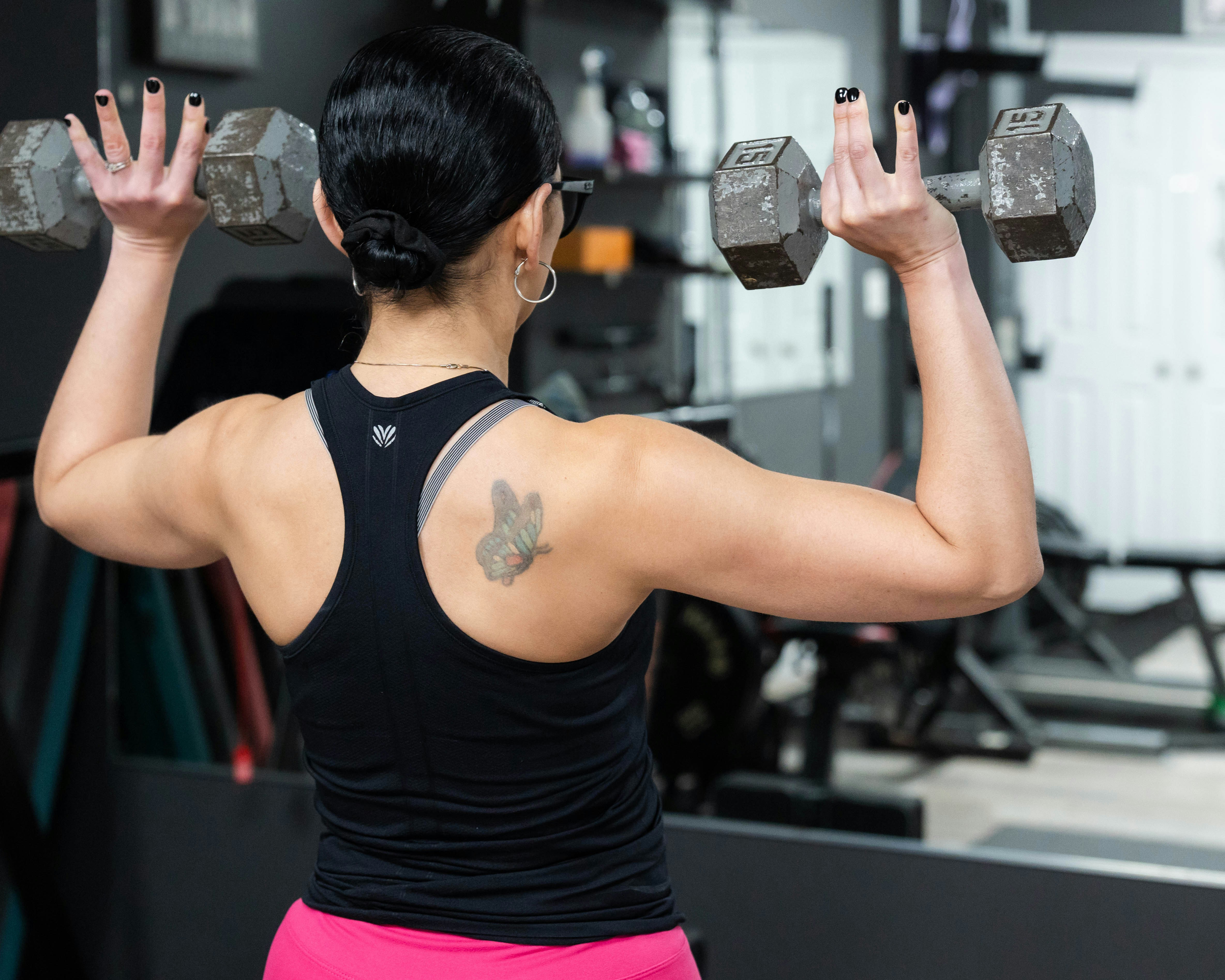 Woman exercises with dumbbells, seen from the back.