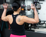 Woman exercises with dumbbells, seen from the back.