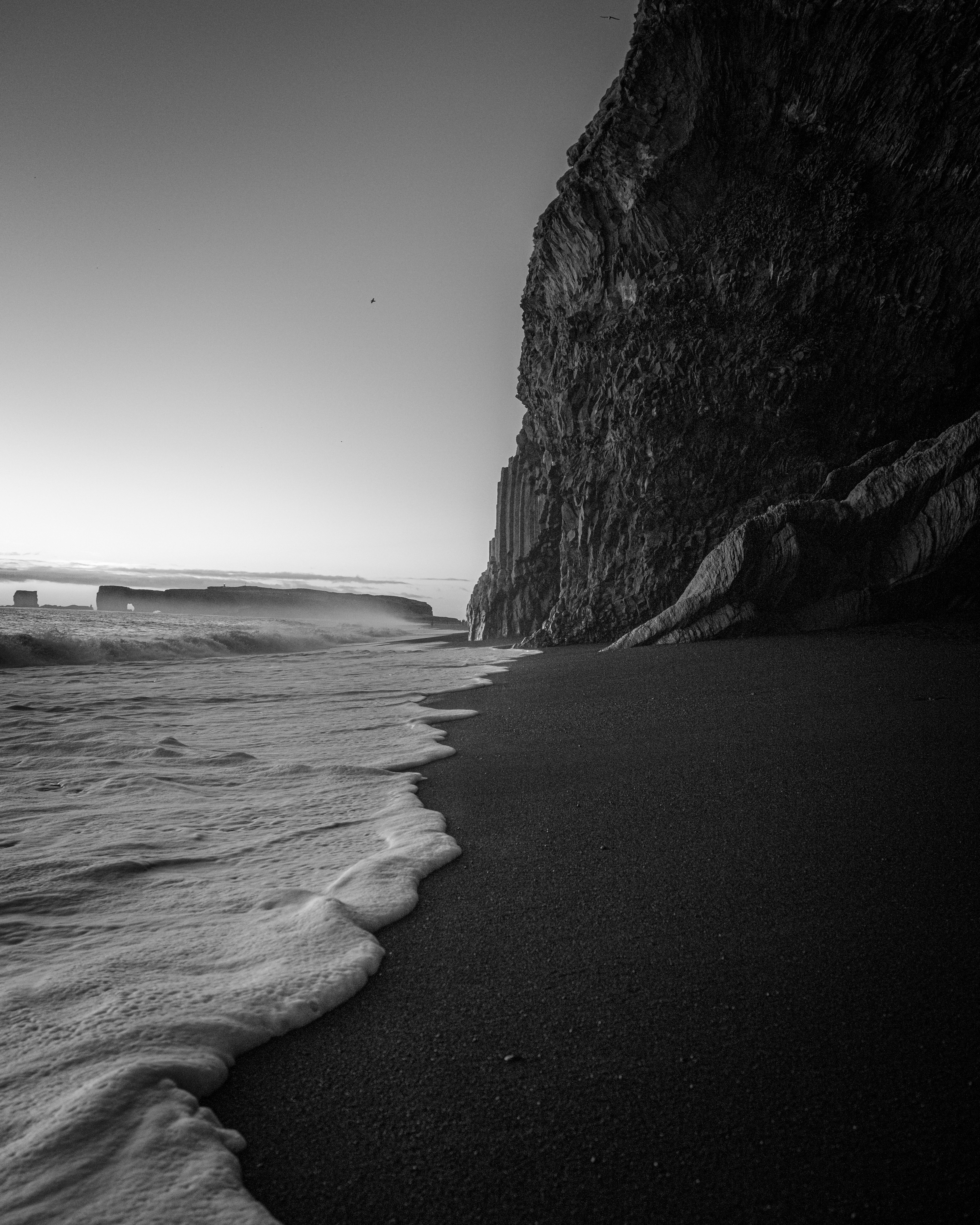 Wellen schlagen an einem dunklen Strand in der Nähe einer Klippe.