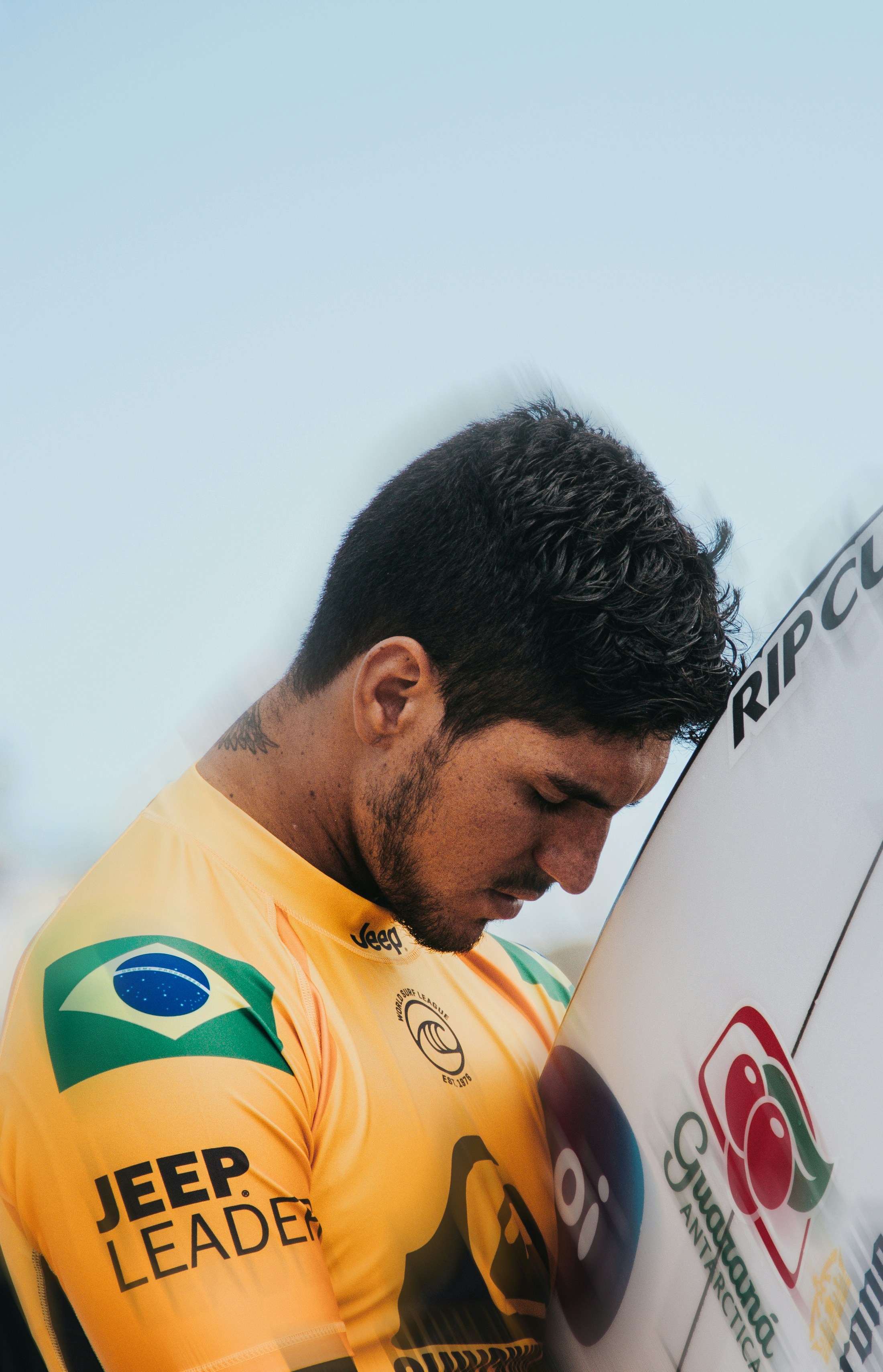 A surfer gazes thoughtfully at his surfboard.