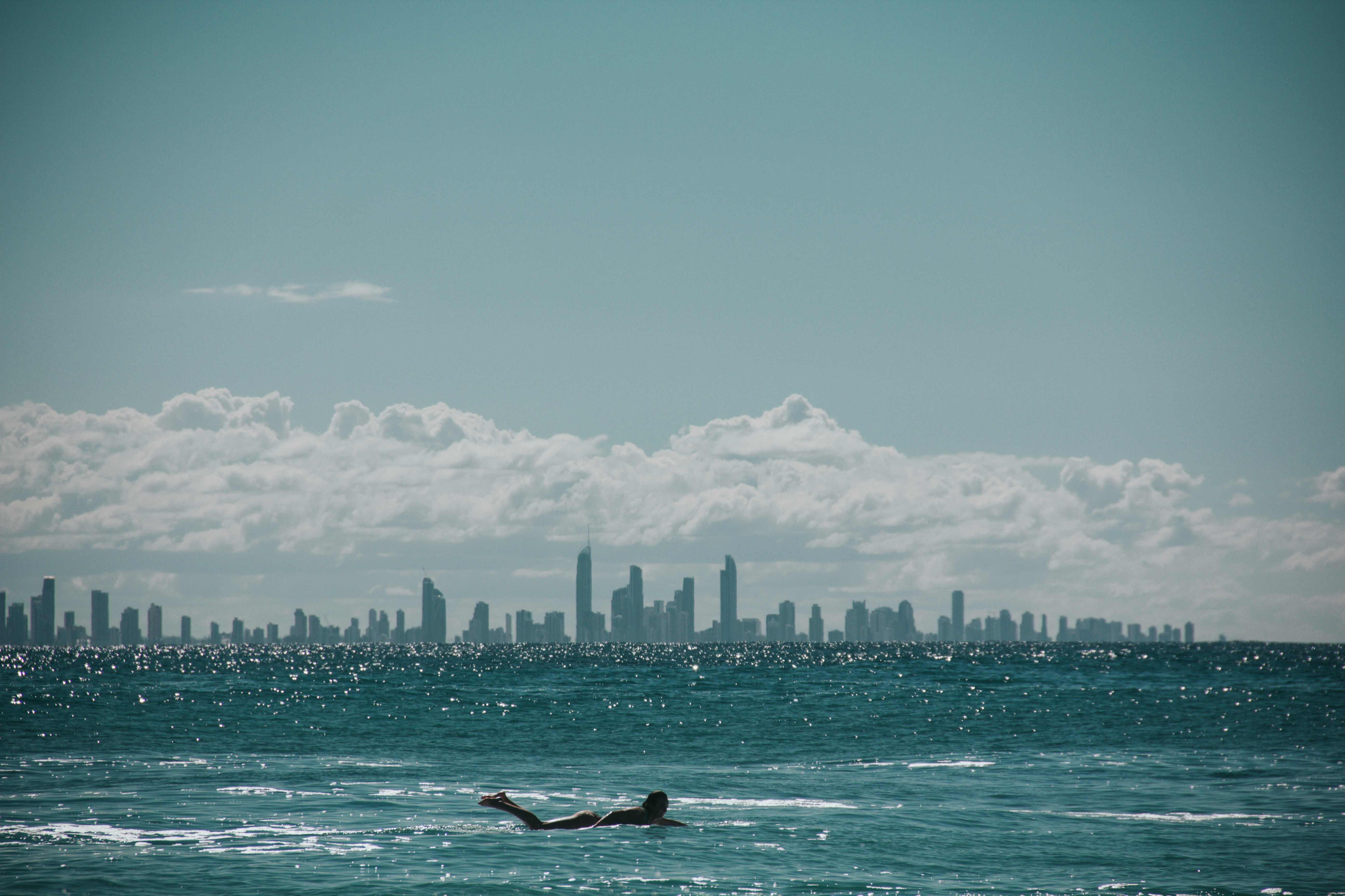 Surfer in the ocean with city skyline in the background., 