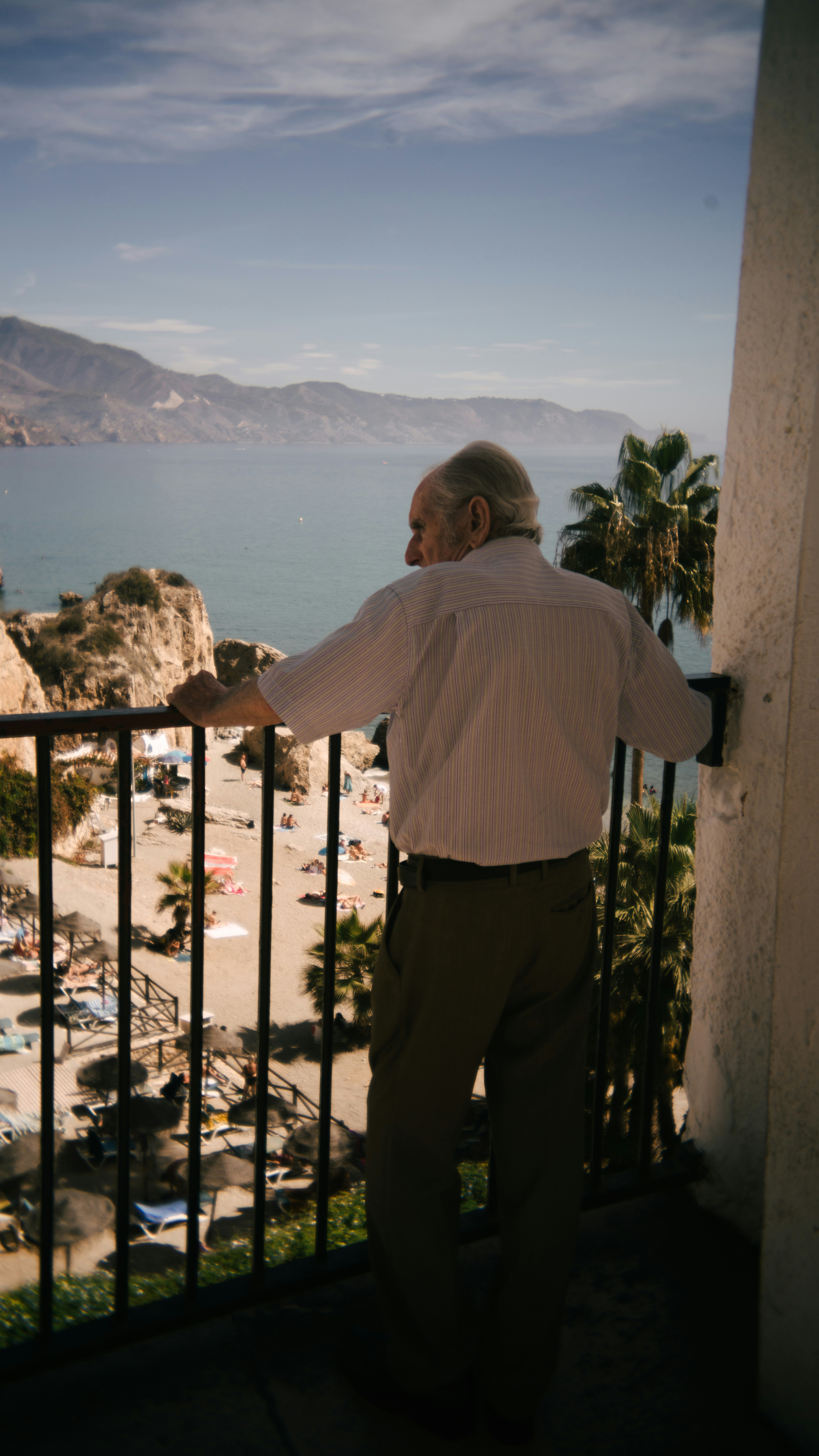An elderly man gazes at the beach from a balcony.