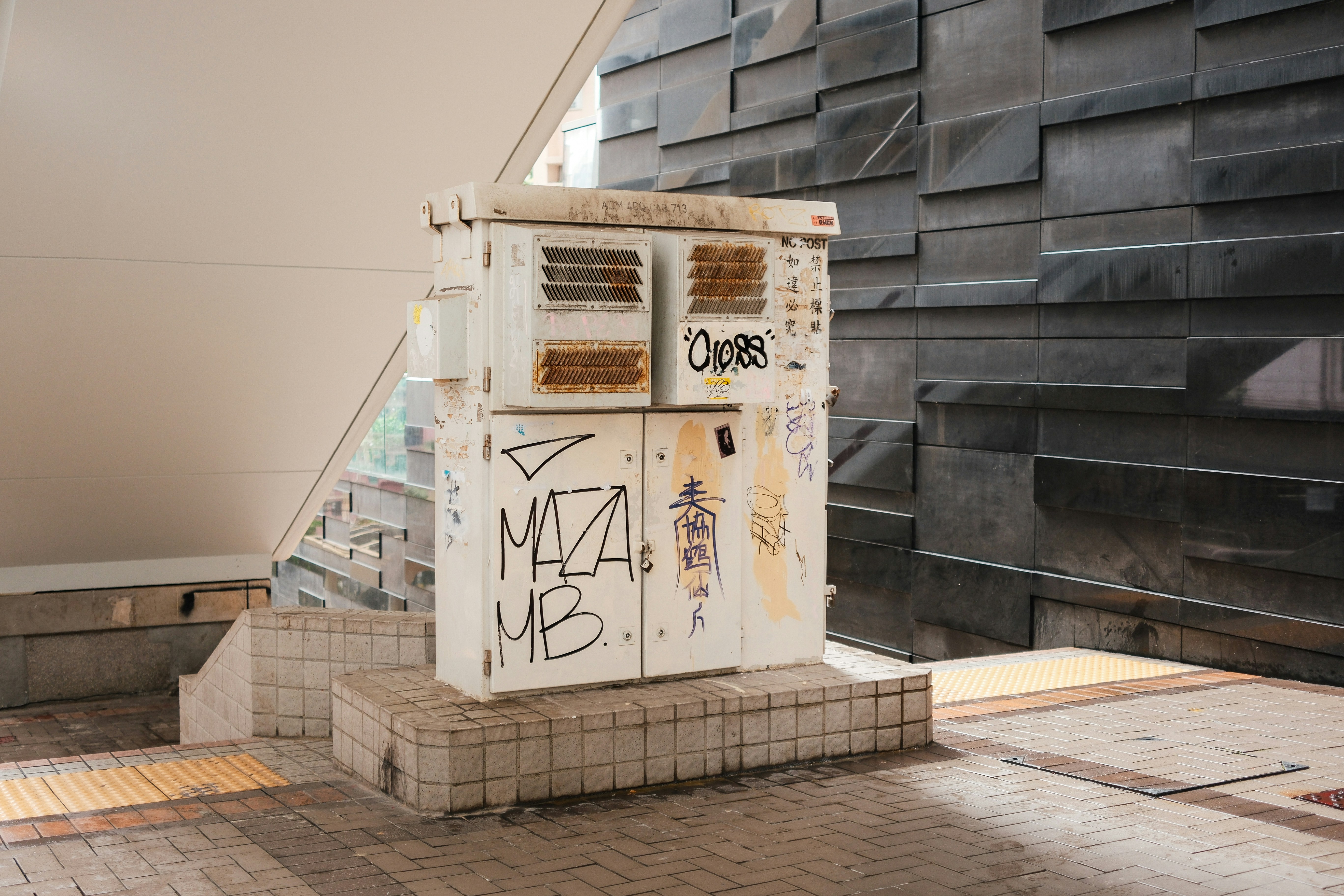 Graffiti-covered electrical box stands near a wall.