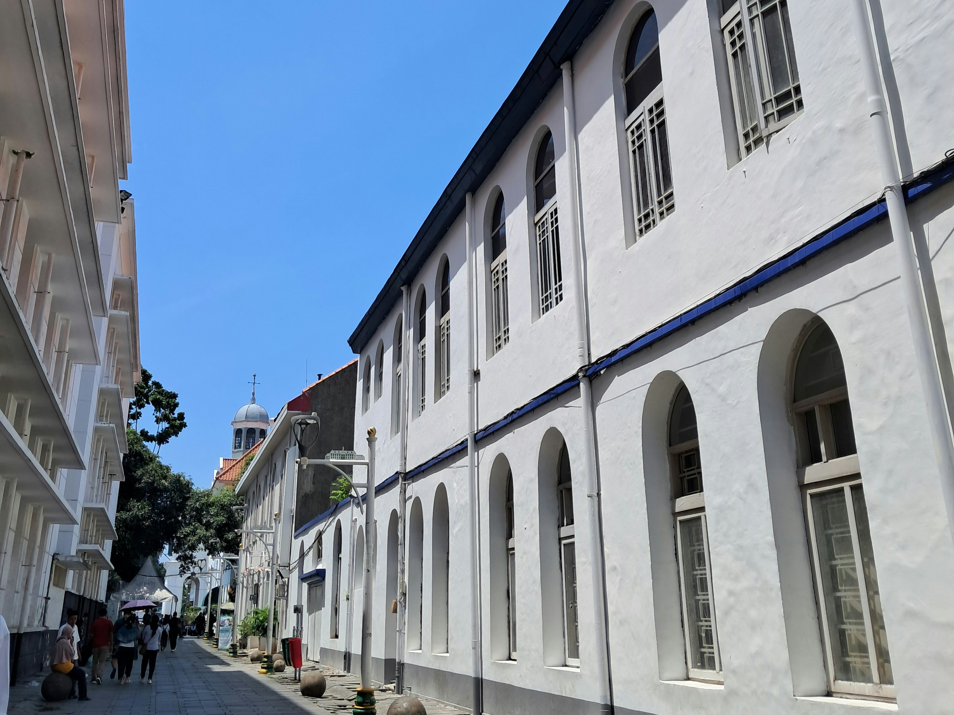 Buildings line a narrow street under a sunny sky.