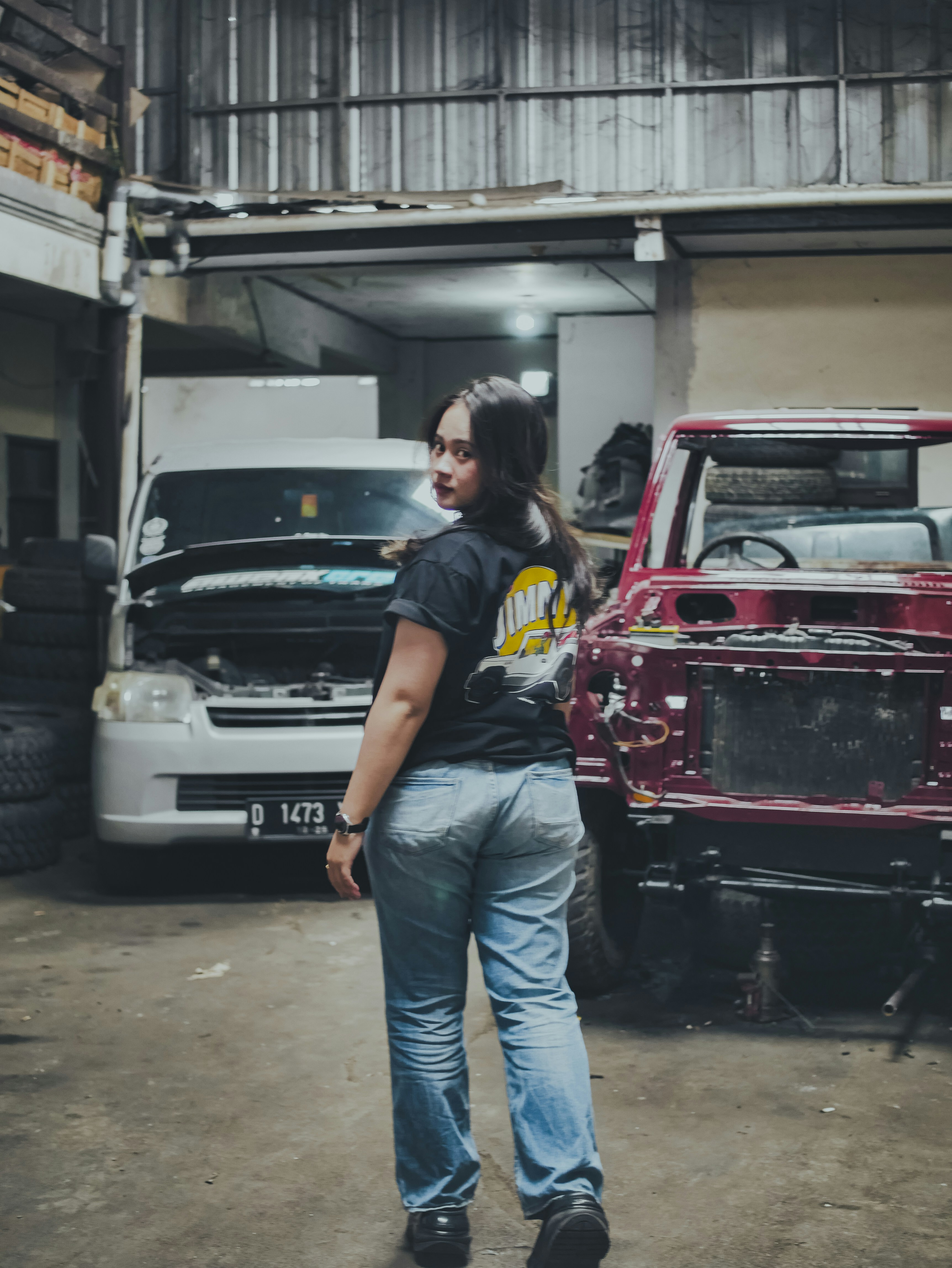 Seorang wanita berdiri di garasi perbaikan mobil.