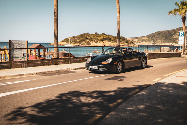 A black sports car drives along a sunny road