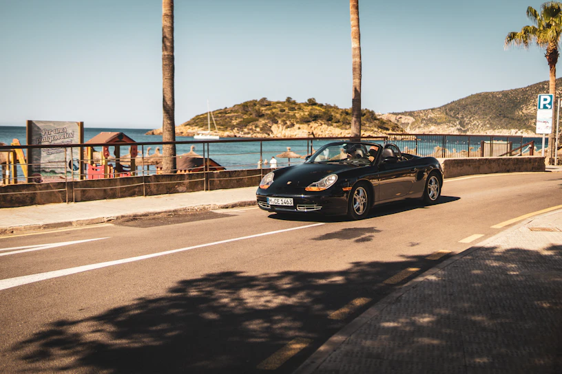 A black sports car drives along a sunny road