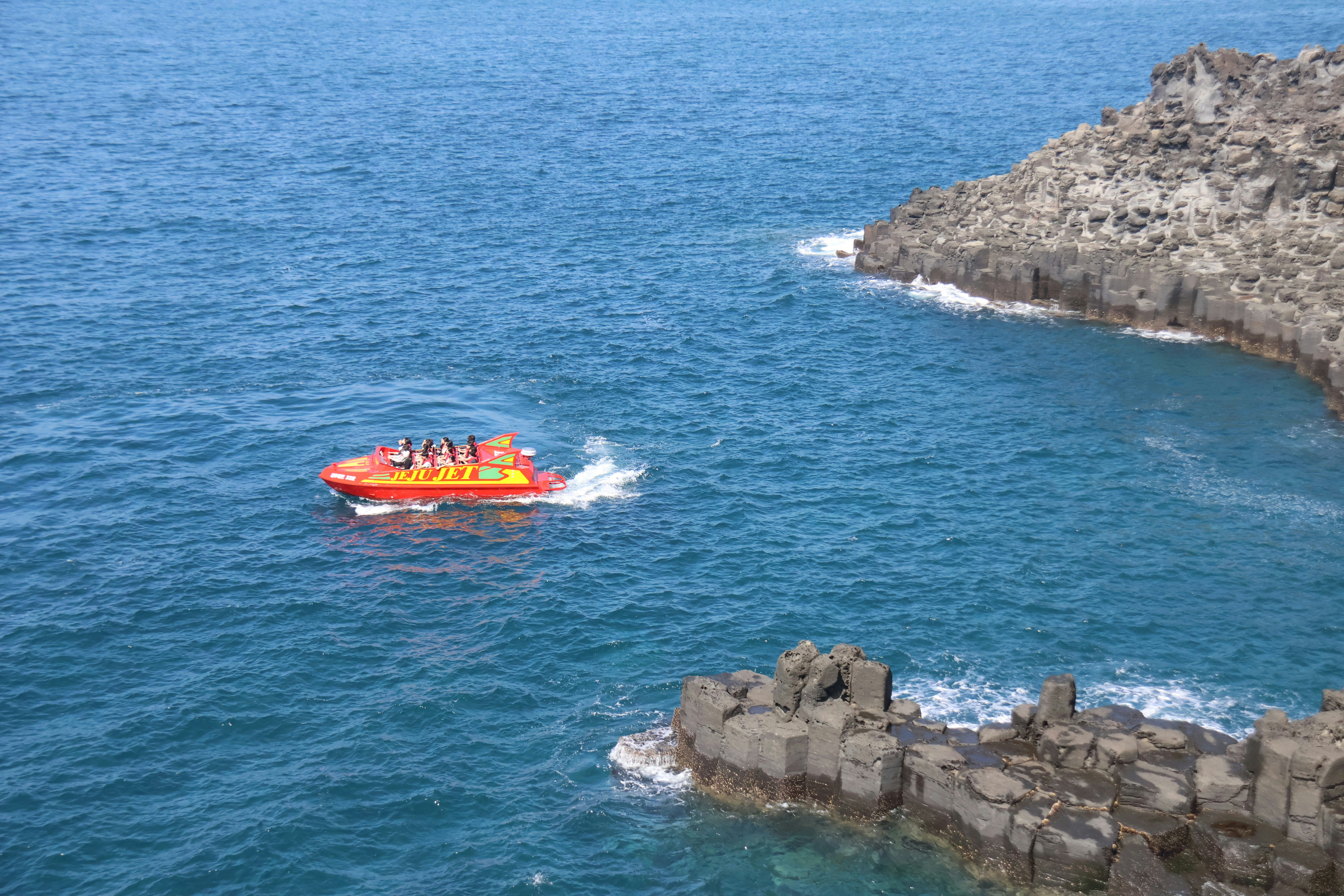 A boat rides near a rocky shore.
