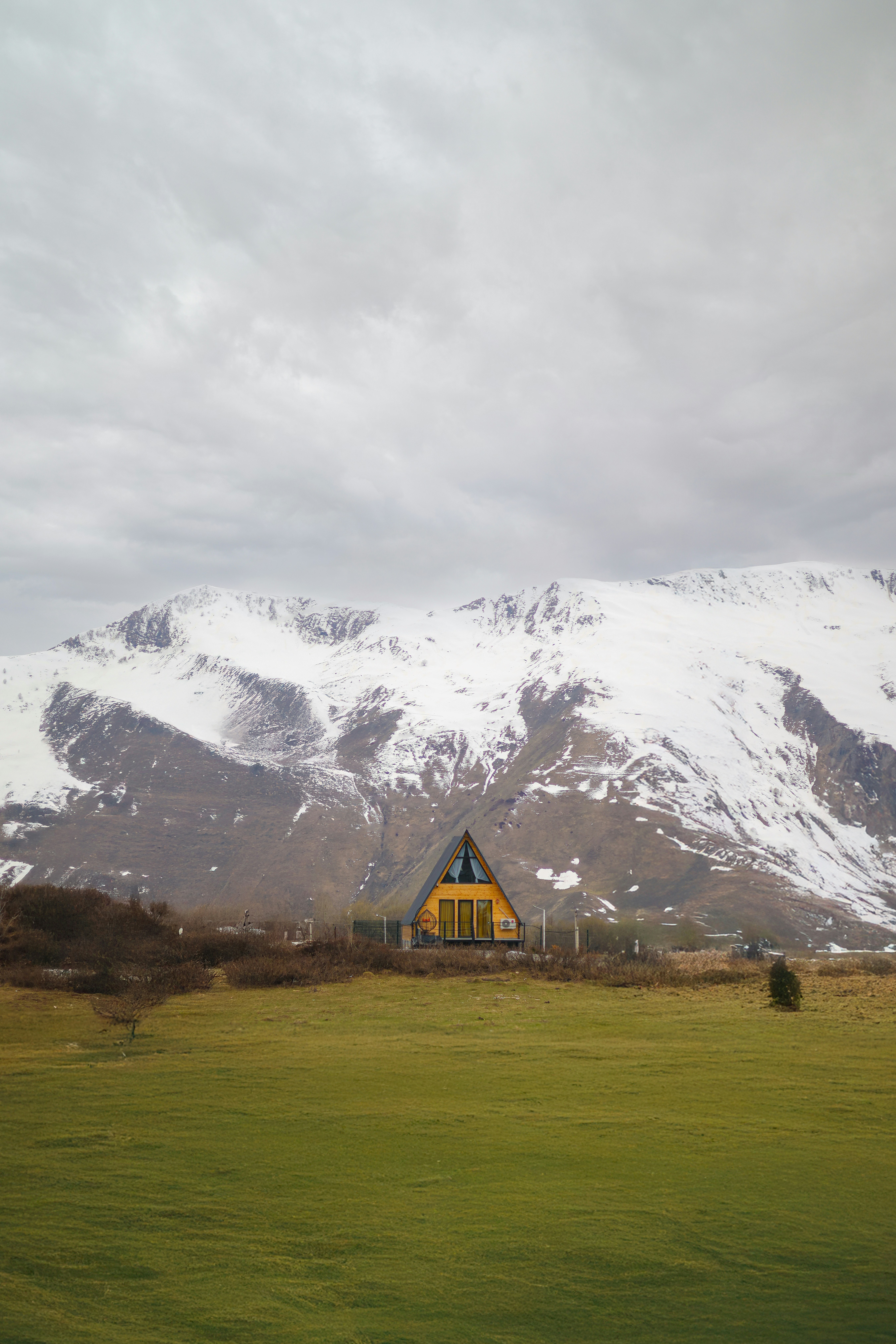A yellow a-frame house sits before mountains.