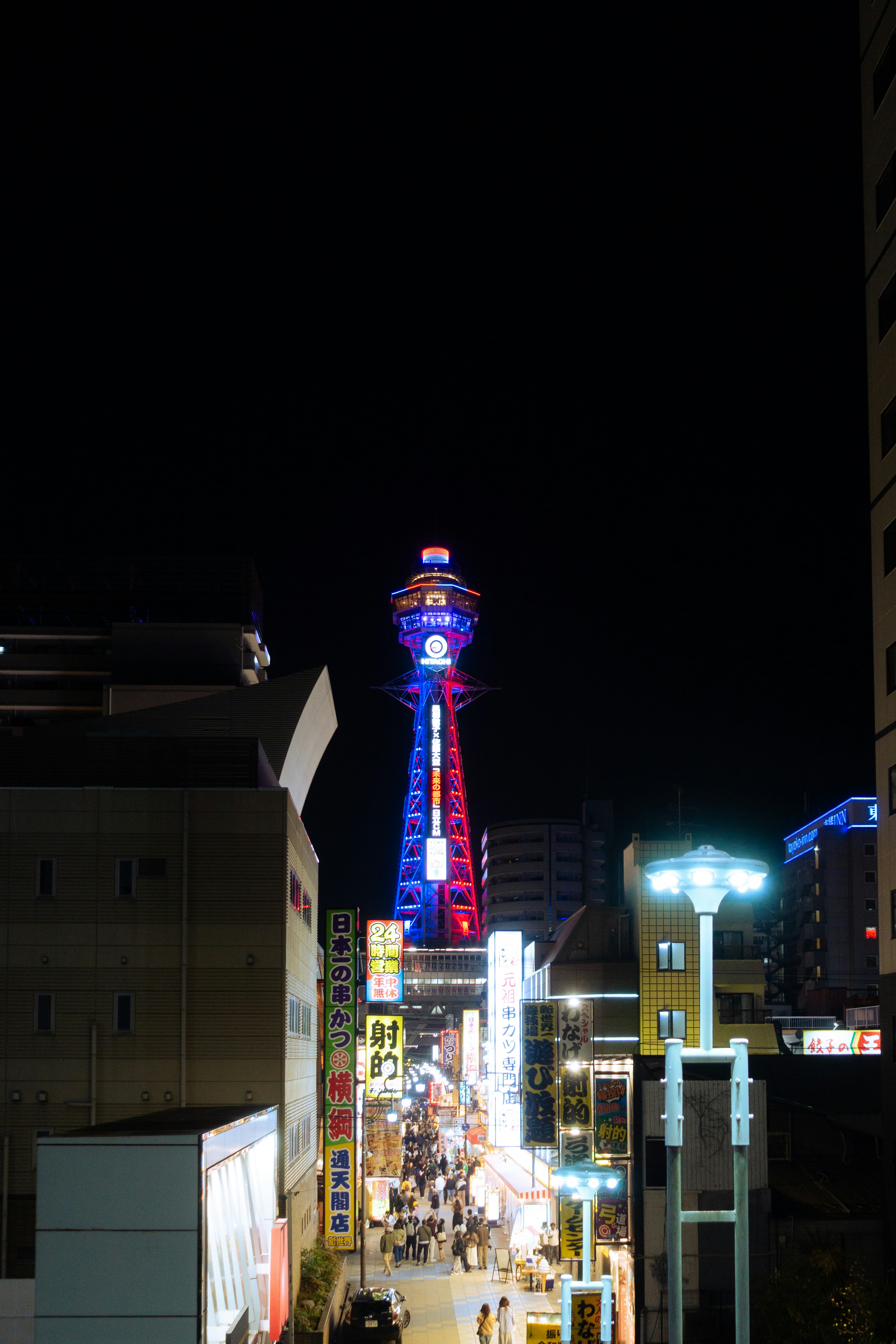 A lit-up tower overlooks a lively street at night.