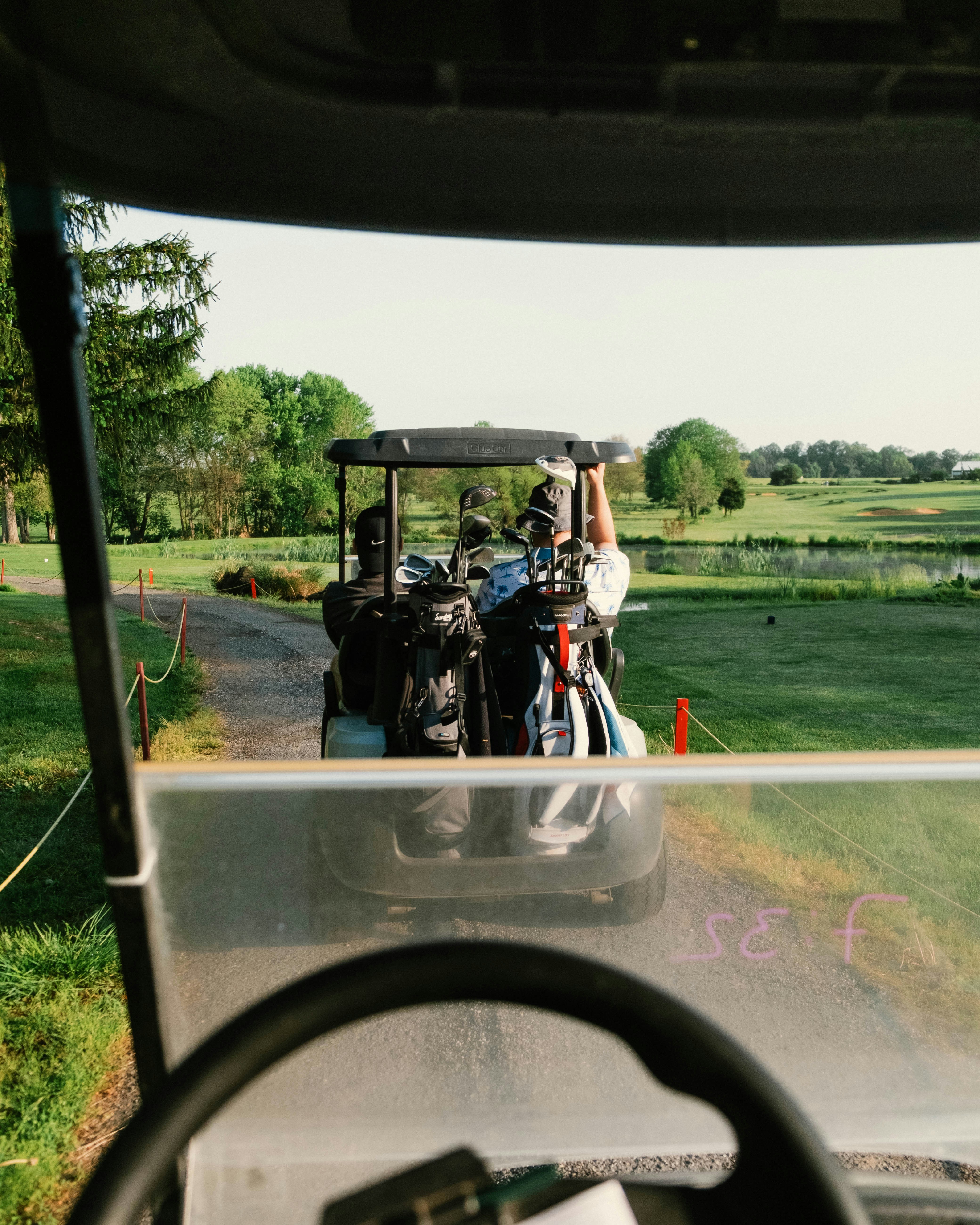 Golf cart heads down the fairway on a sunny day.