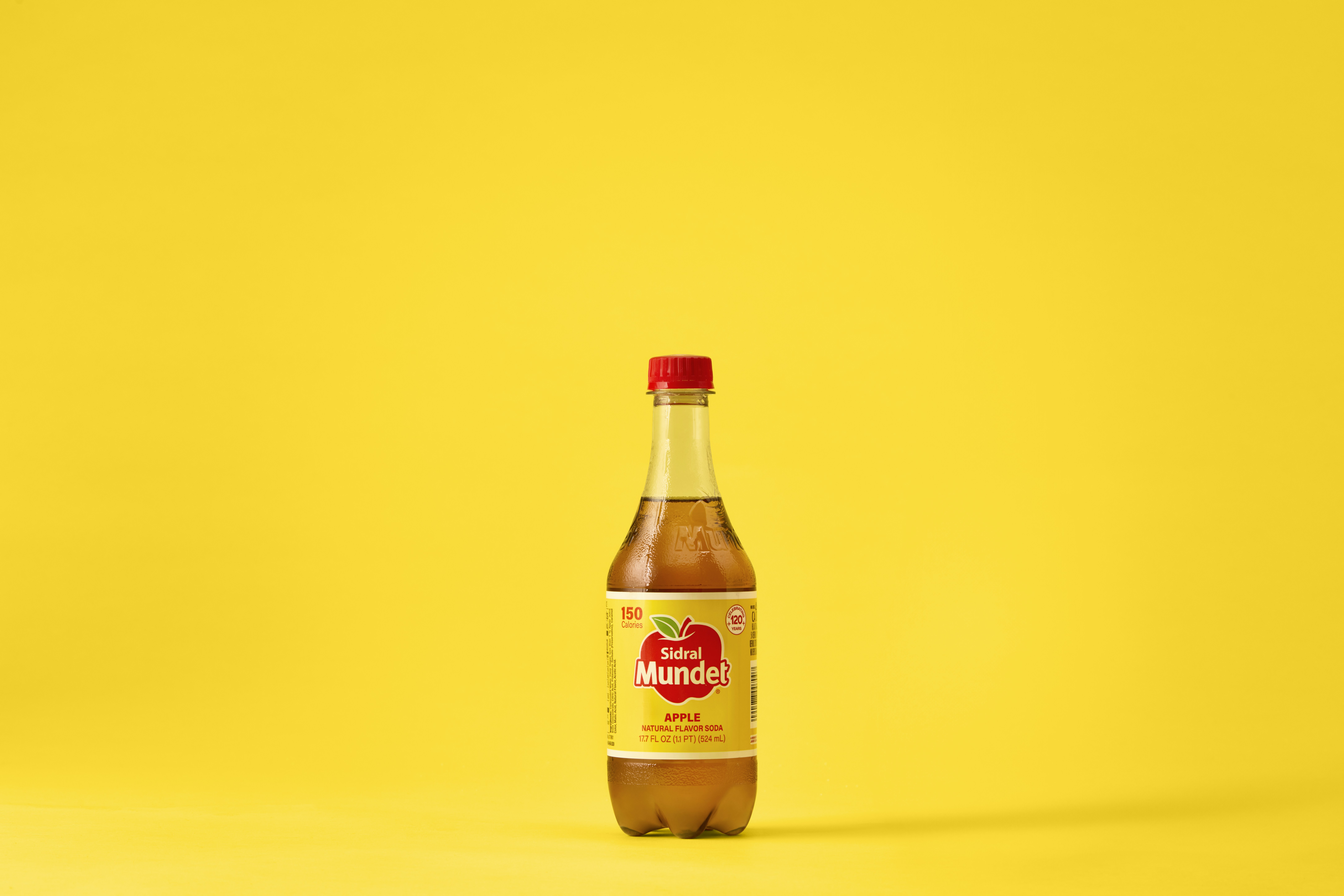 A bottle of apple juice sits on a yellow background.