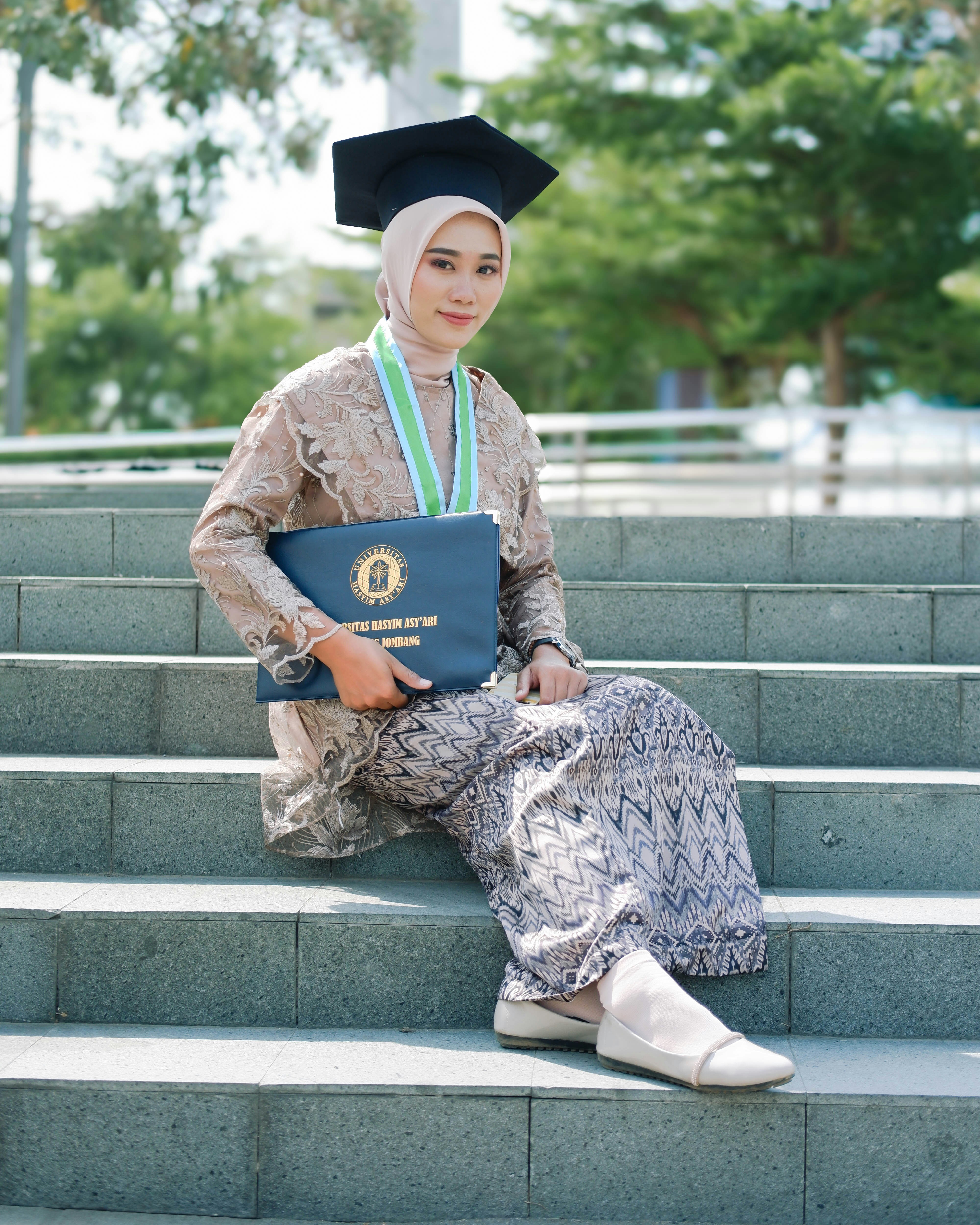 Seorang lulusan duduk dengan bangga dengan ijazah di tangga.