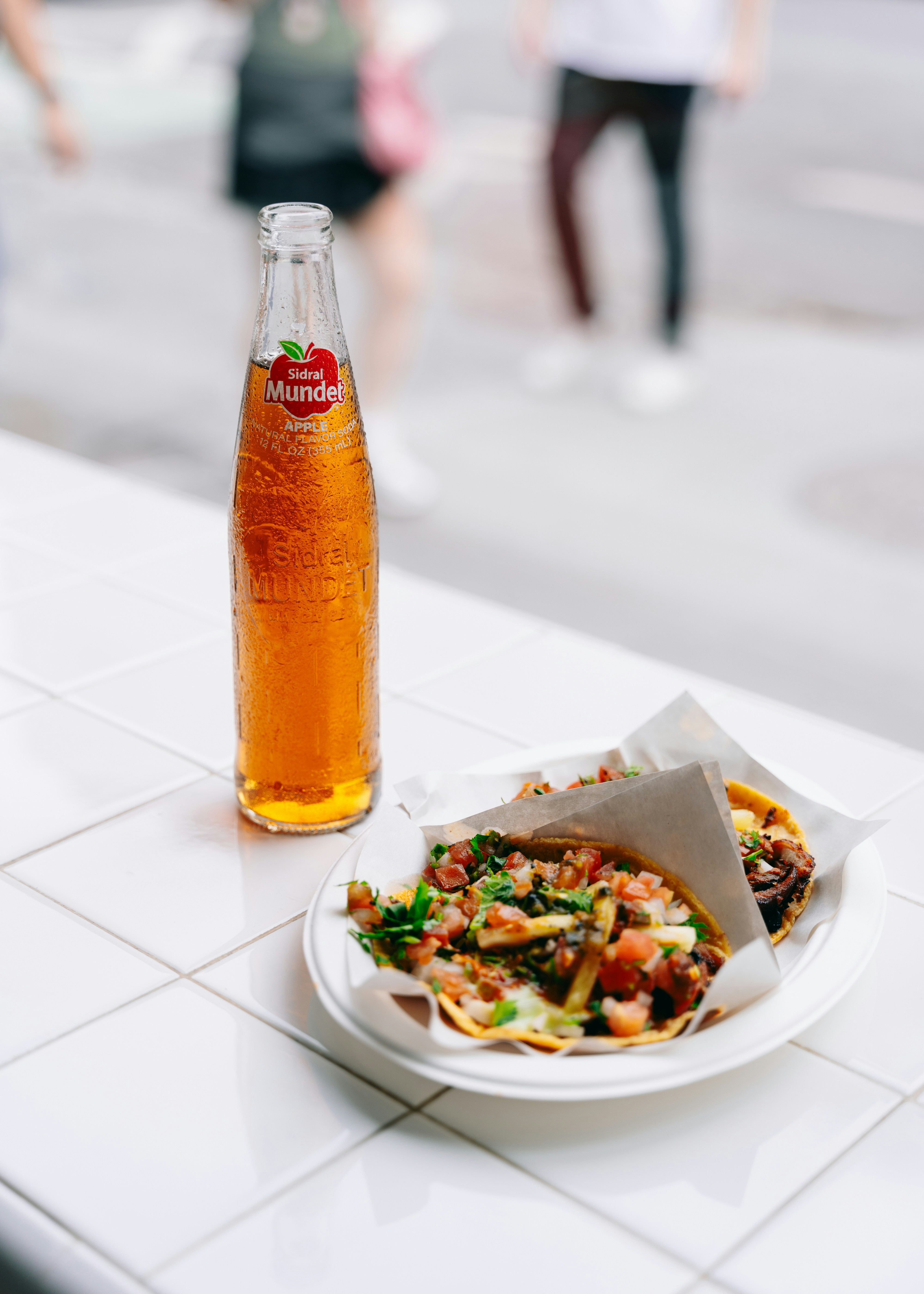 Tacos and a bottle of cider on a white table.