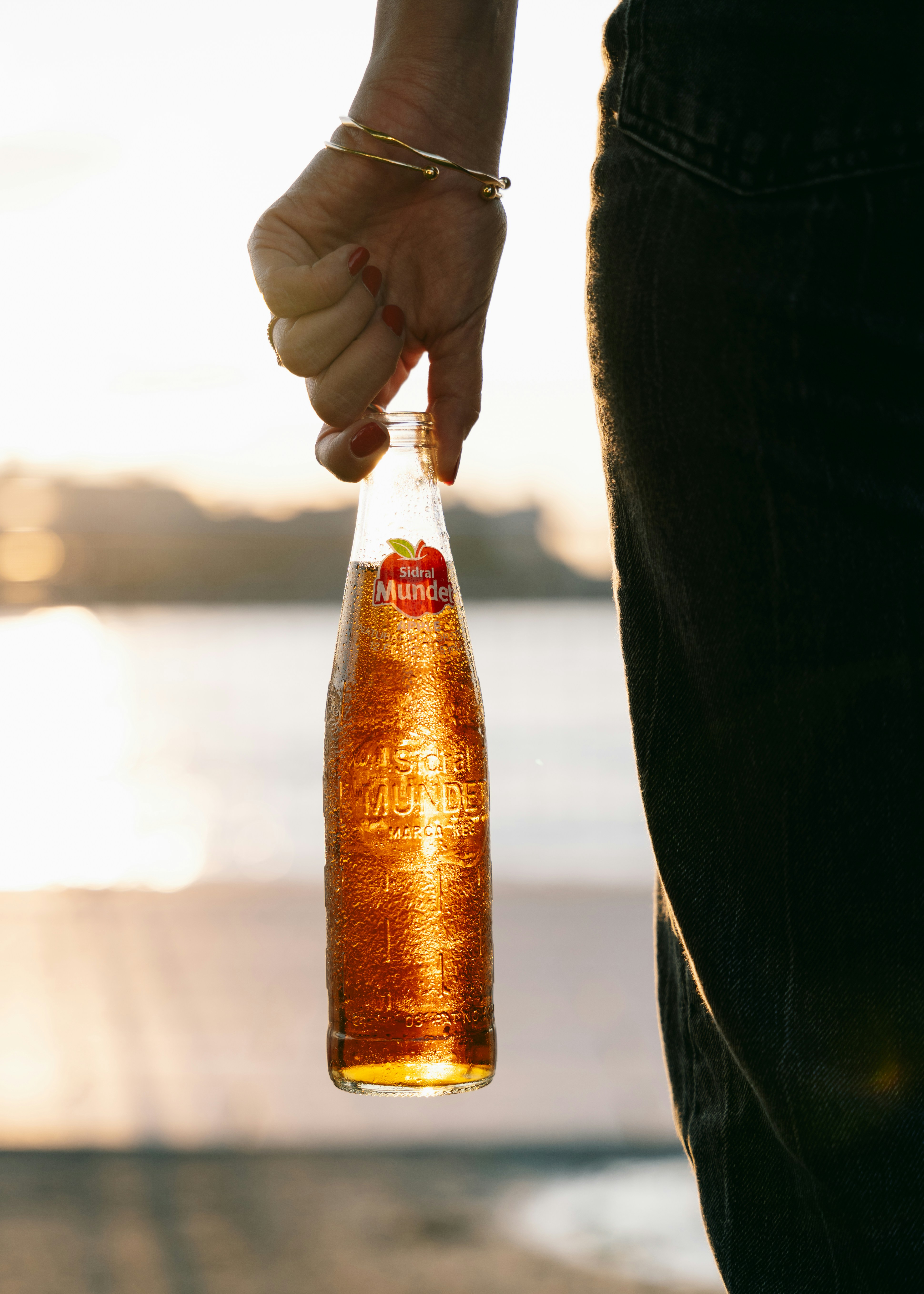 A hand holds a glowing bottle of beer.