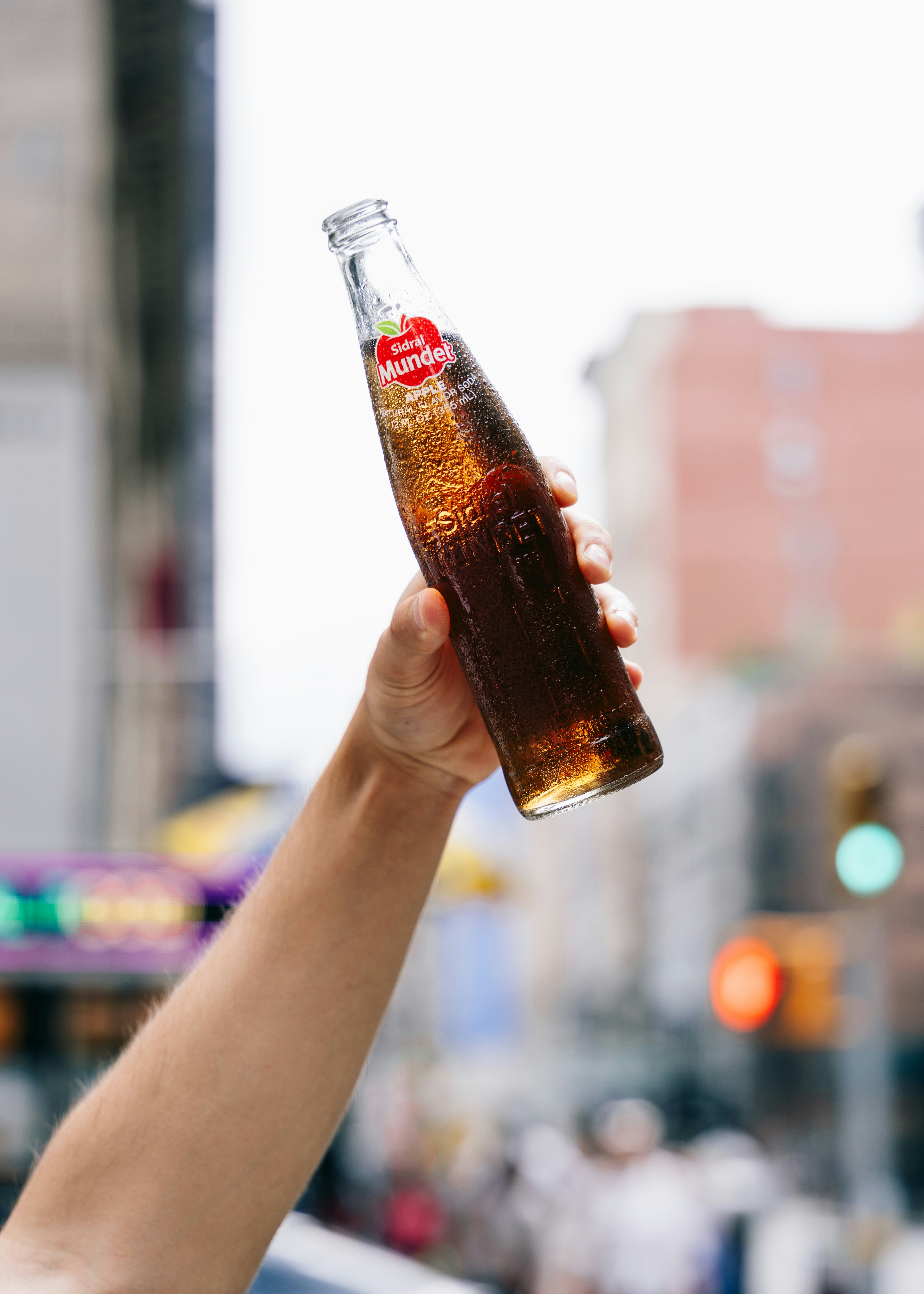 A hand holds up a glass bottle of soda.