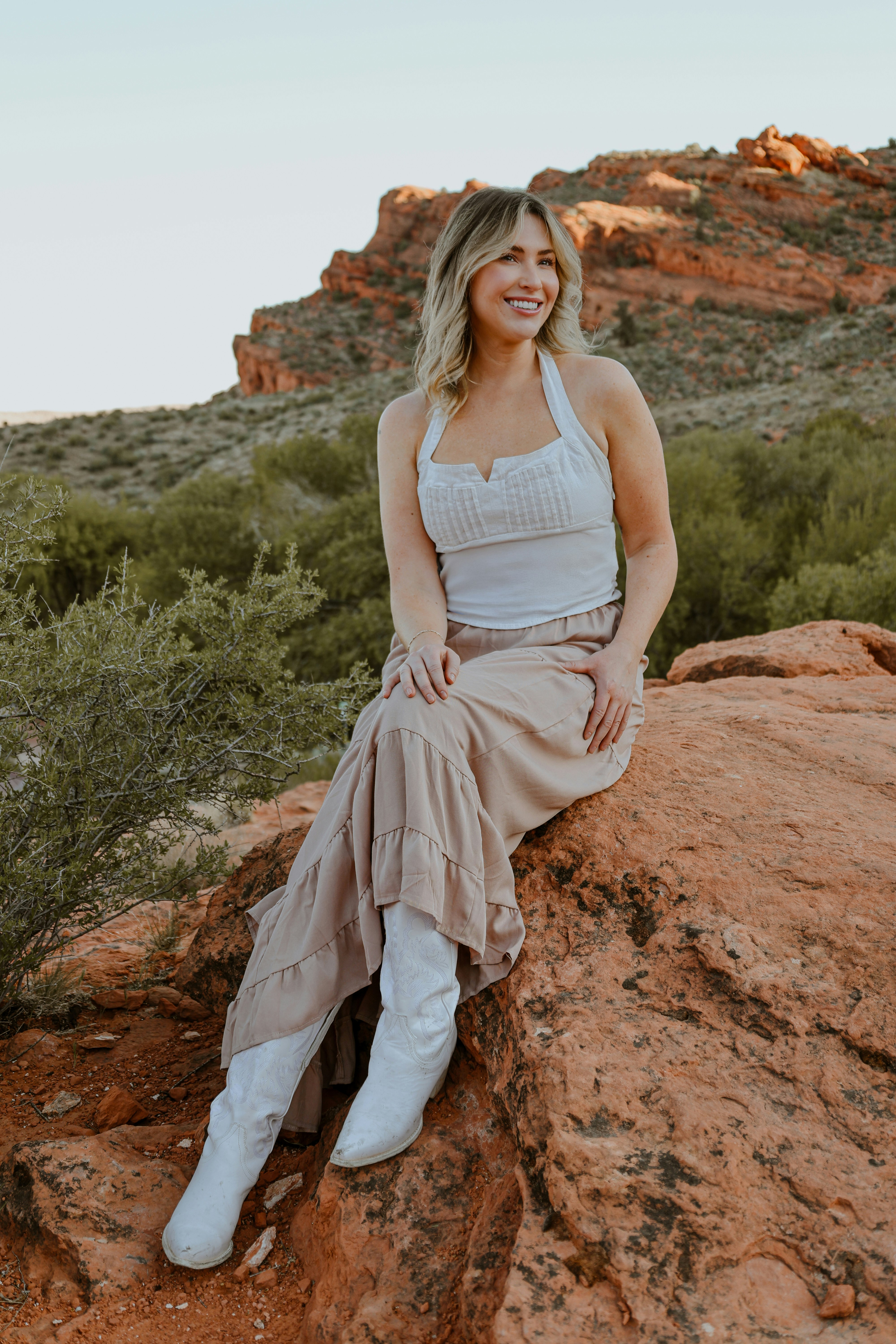Woman smiles while sitting on a red rock
