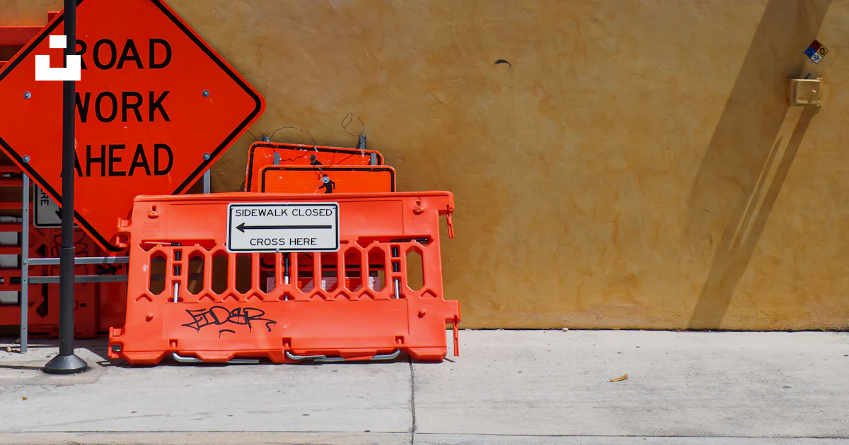 Road work signs stand beside a brown wall. photo – Free Usa Image on ...