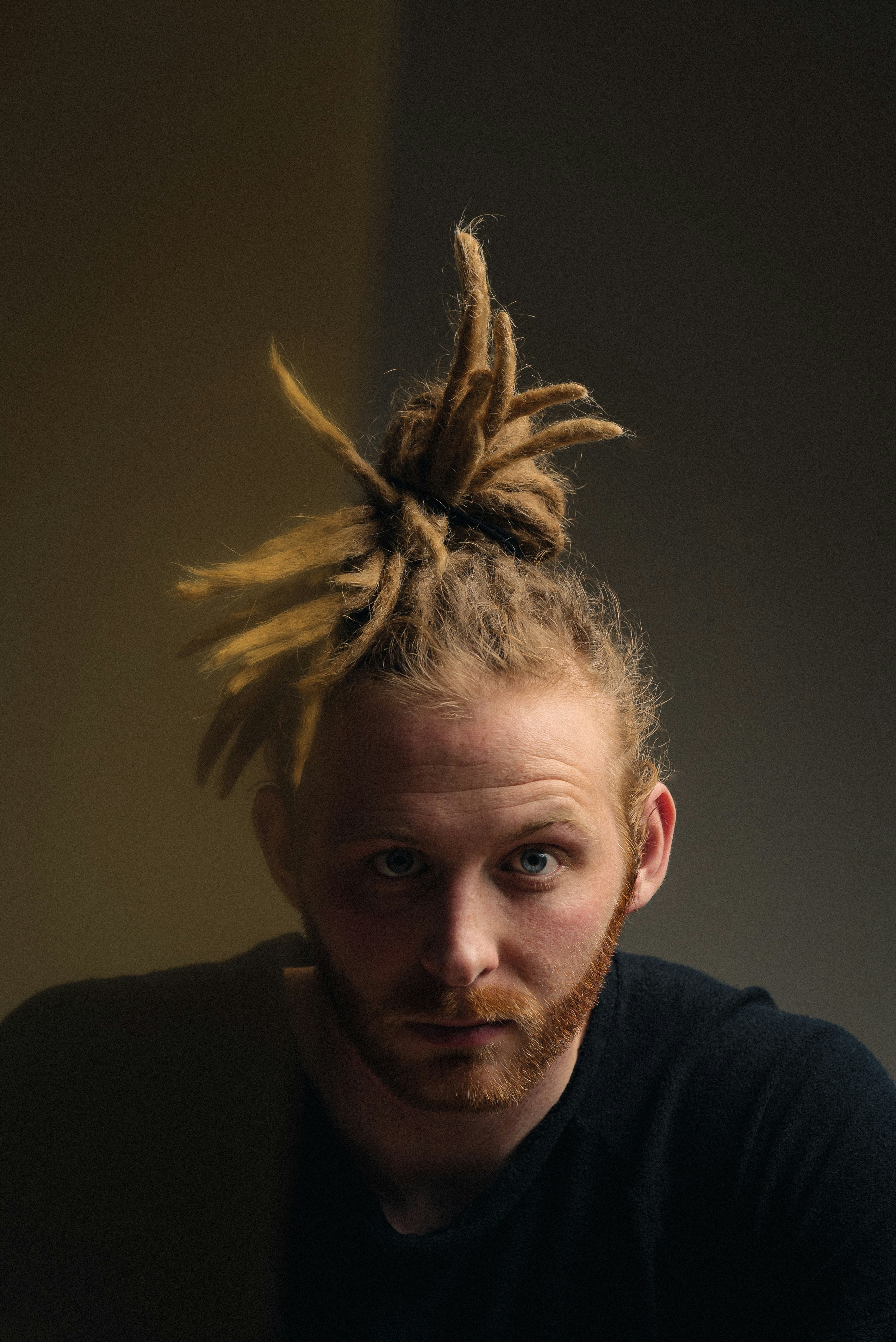 A man with dreadlocks is looking directly at camera.