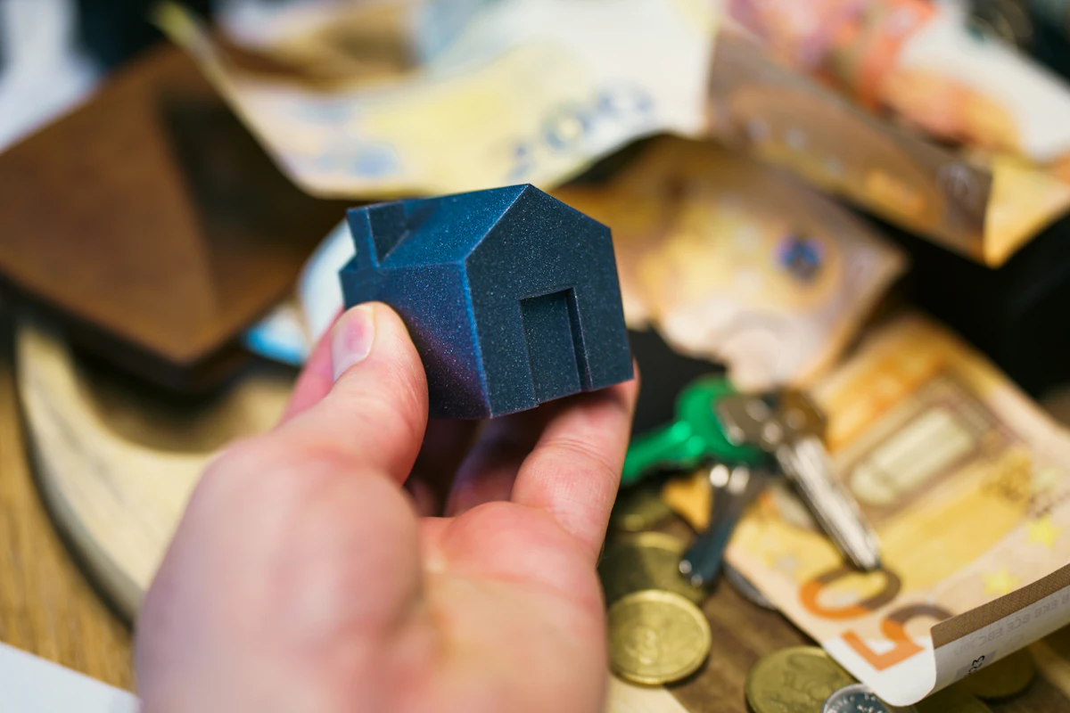A small model house beside a door key and stacked coins