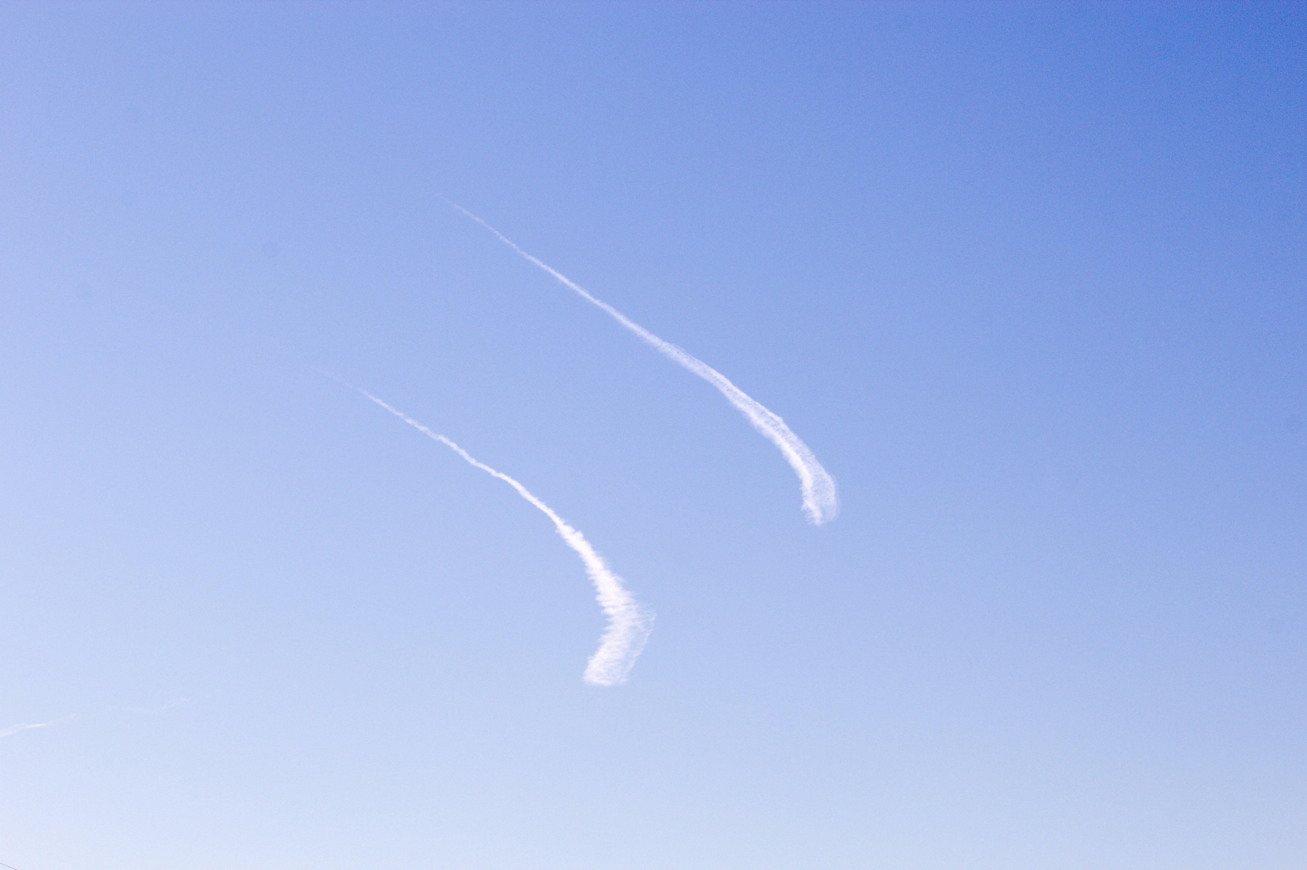 Two contrails streak across a clear blue sky.