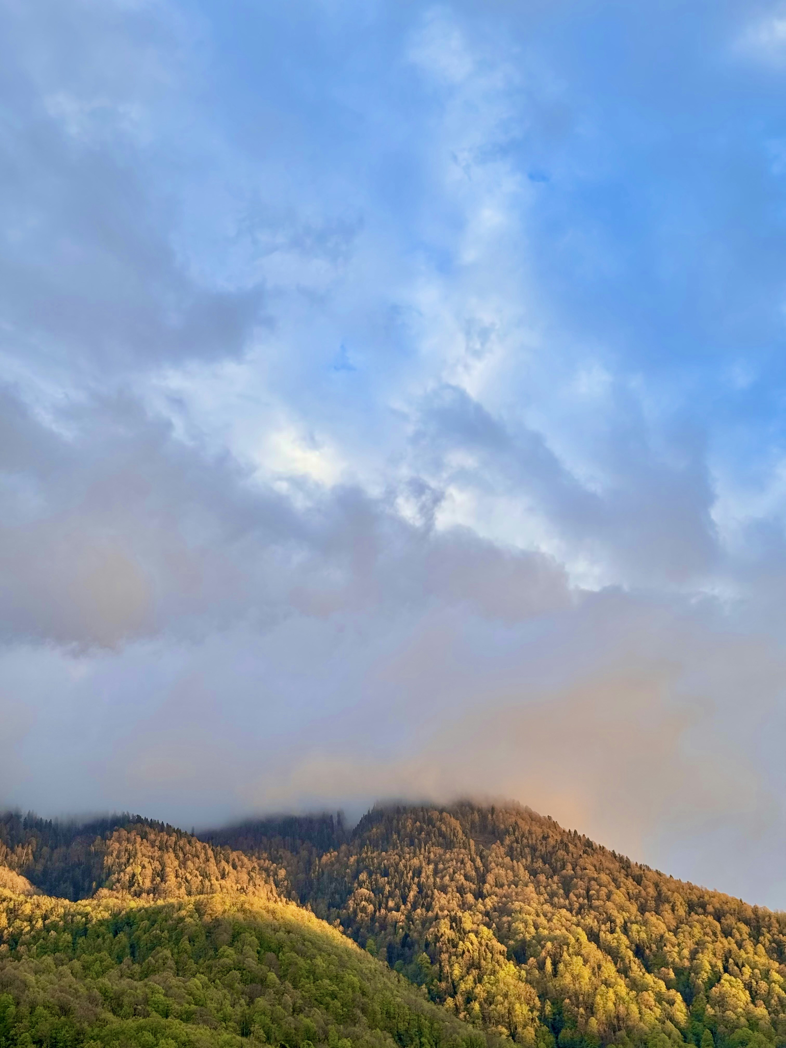 Mountains are lit by the sun, shrouded in clouds.