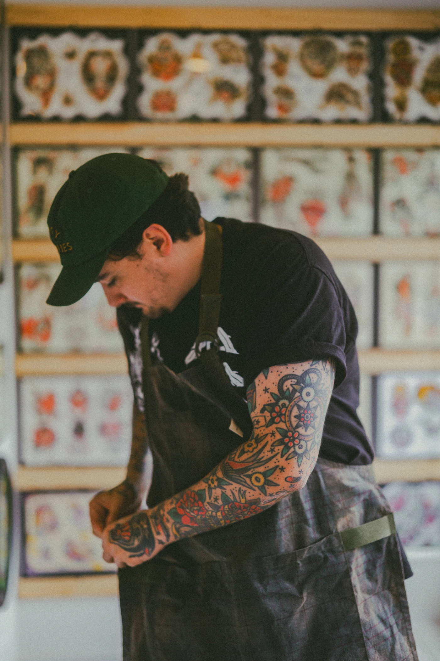 Tatuador de boné trabalhando no estúdio, com flashes de tatuagem na parede